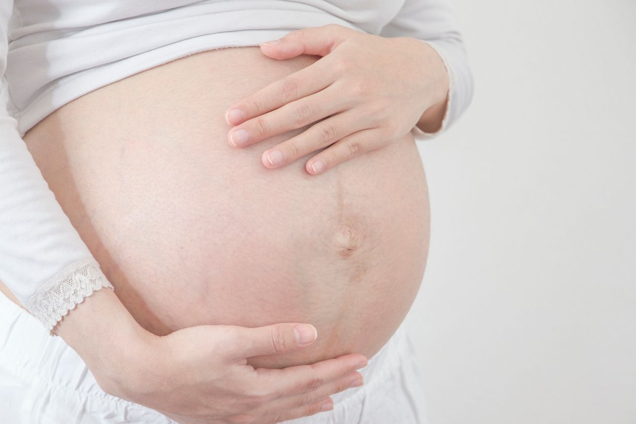 Pregnancy woman shows her belly with isolated gray background.