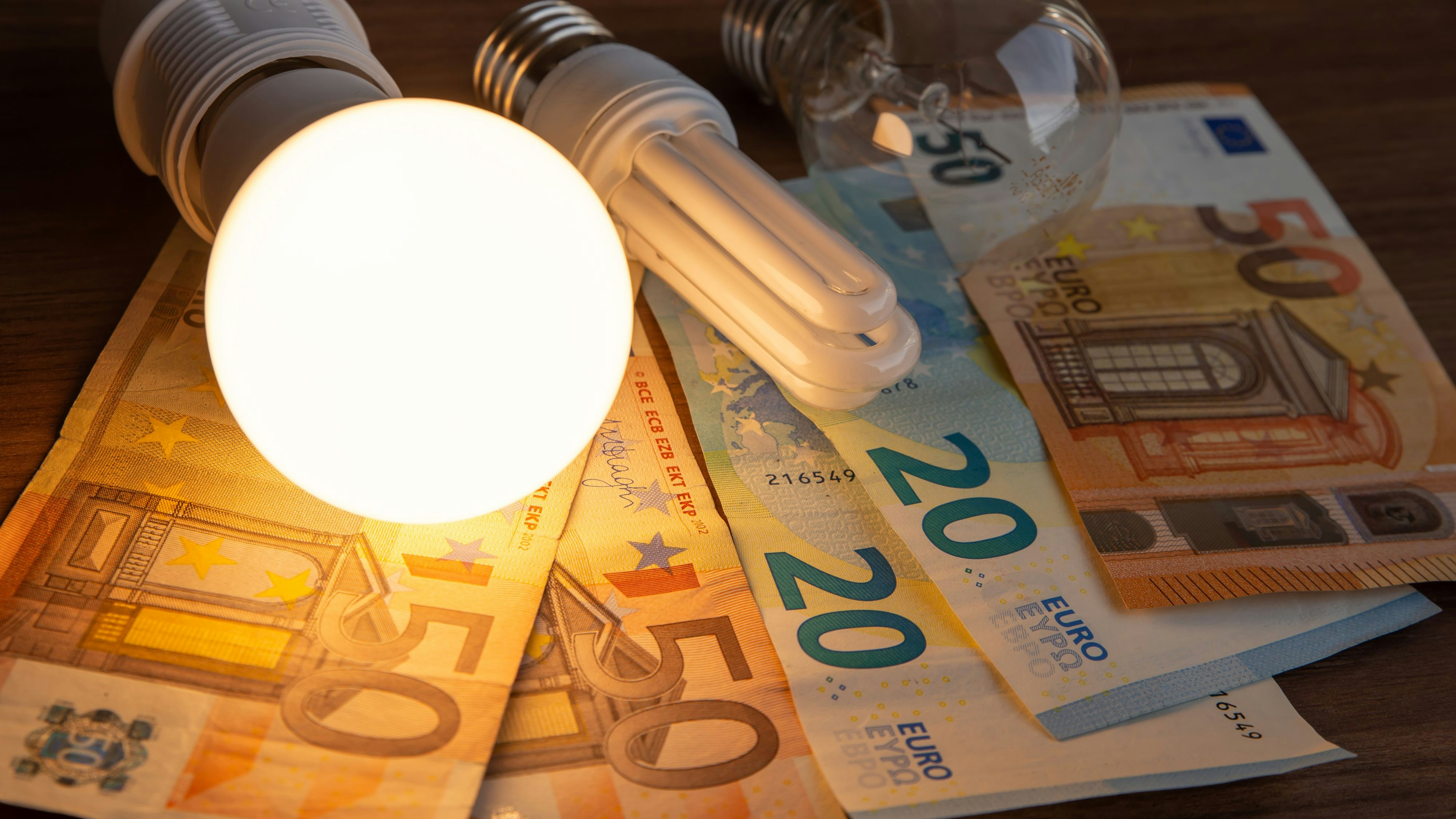 LED bulb on, with fluorescent bulb and incandescent bulb, with bills and coins next to it. Energy costs and evolution of light bulbs.