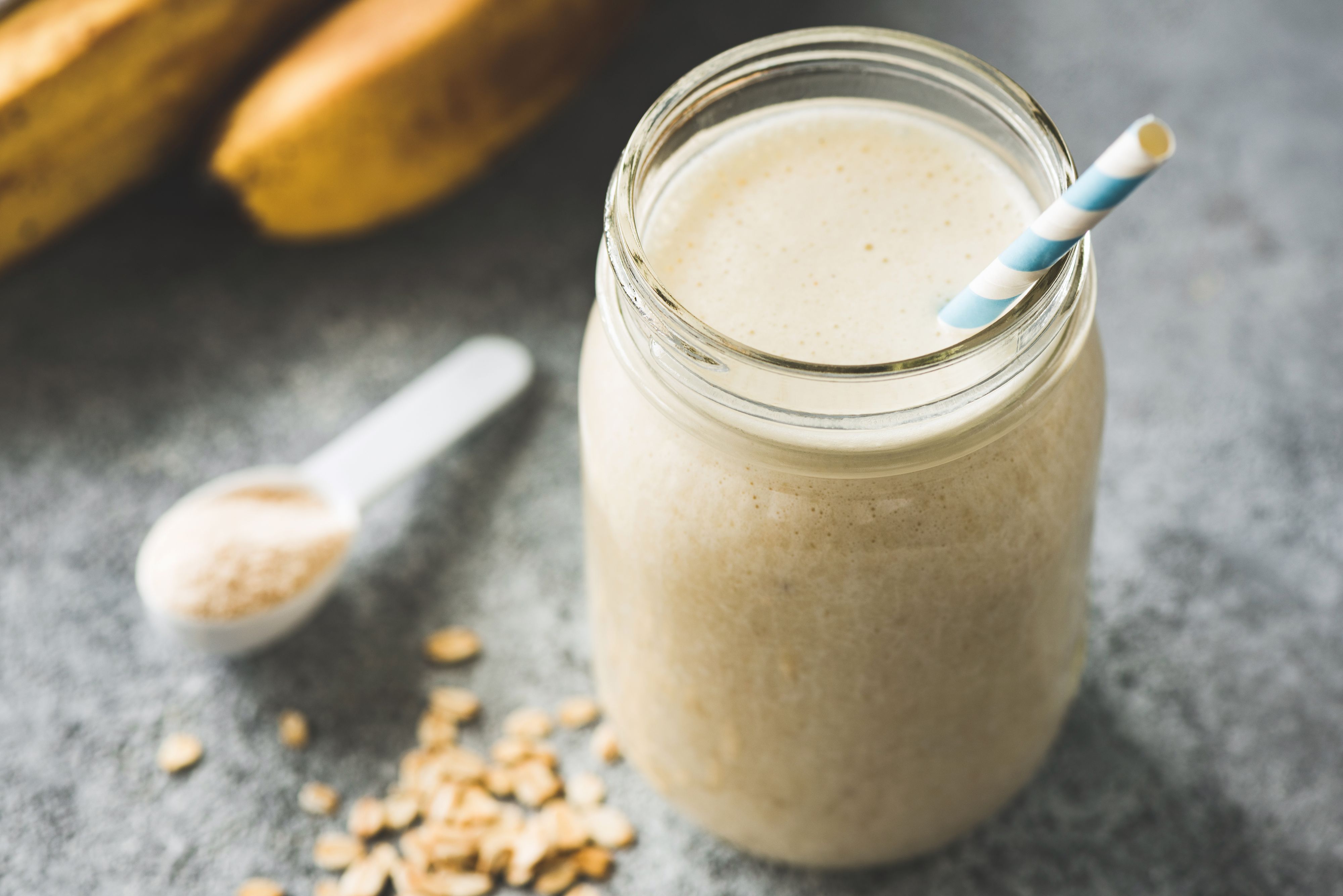 Protein Milkshake With Oats, Banana in jar with paper drinking straw on concrete background. Closeup view, selective focus. Concept of vegan sporty healthy lifestyle
