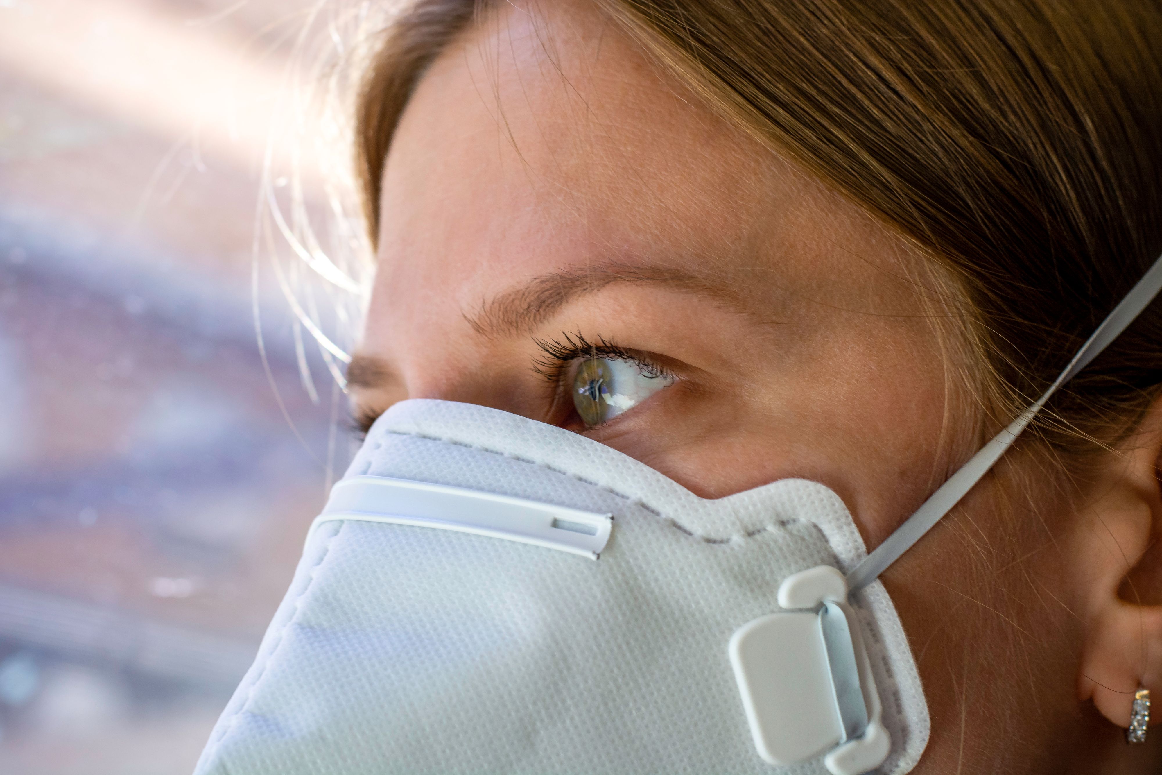 Close up woman wearing a FFP3 face mask looking outside. Disposable respirator protective mouth filter mask. Concept of covid-19 coronavirus.