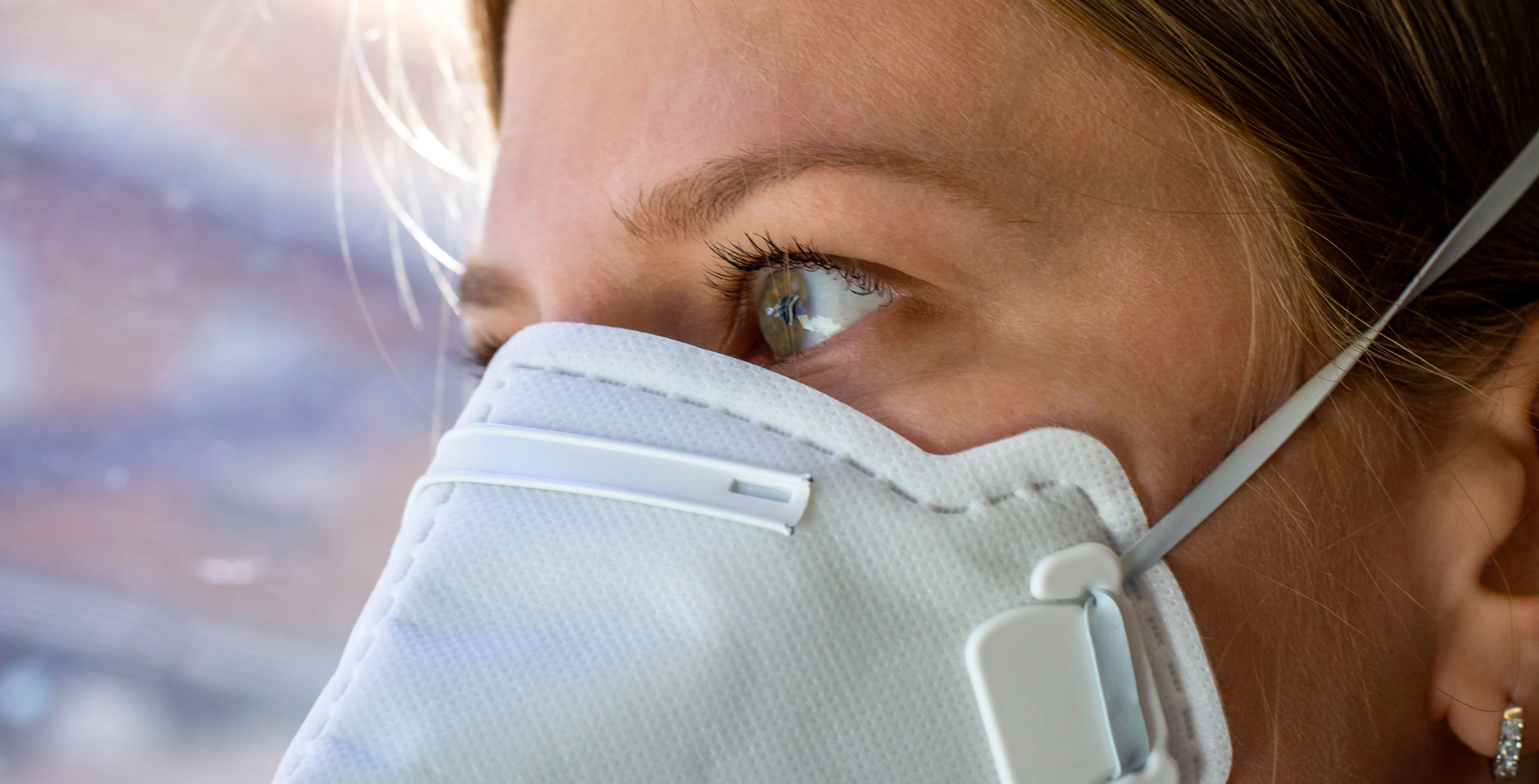 Close up woman wearing a FFP3 face mask looking outside. Disposable respirator protective mouth filter mask. Concept of covid-19 coronavirus.