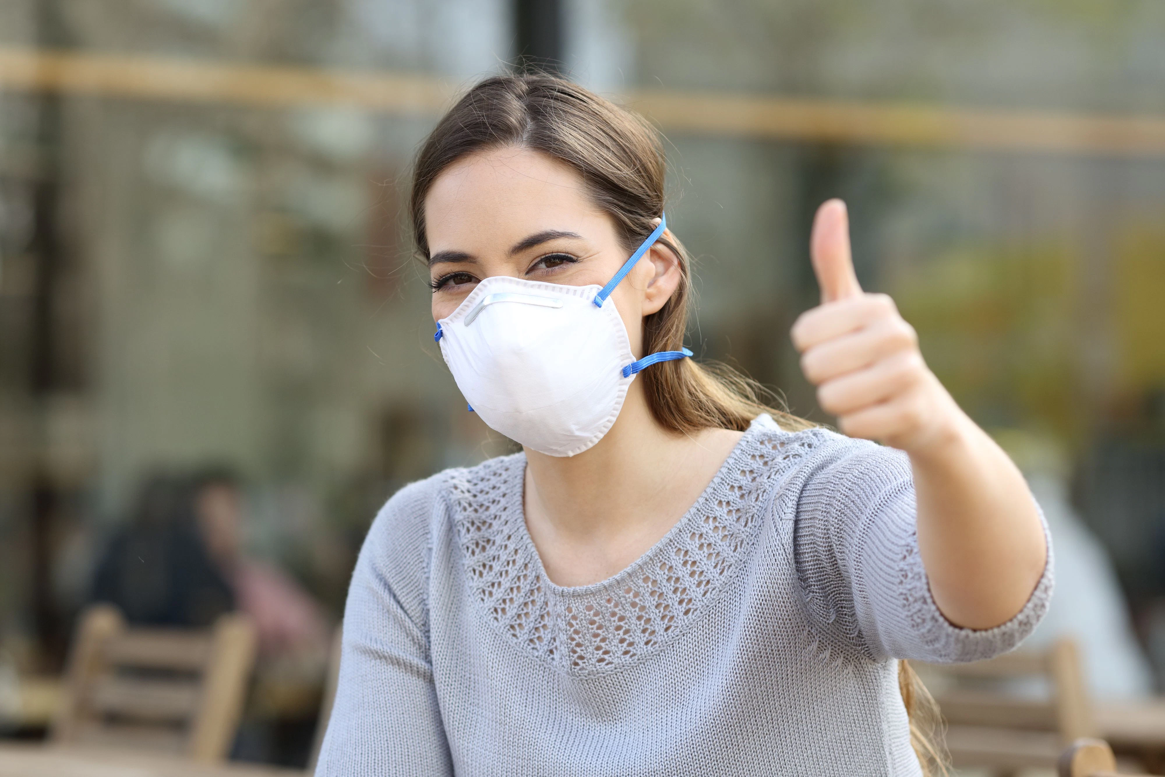 Woman doing thumbs up gesture wearing a protective mask avoiding contagion on a terrace
