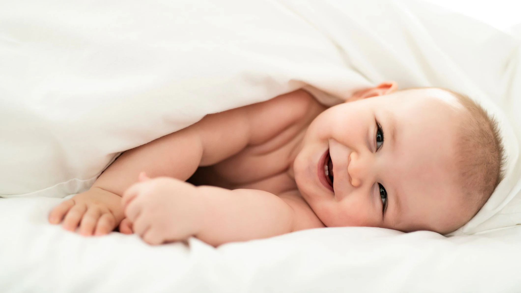 A happy baby lying on white sheet