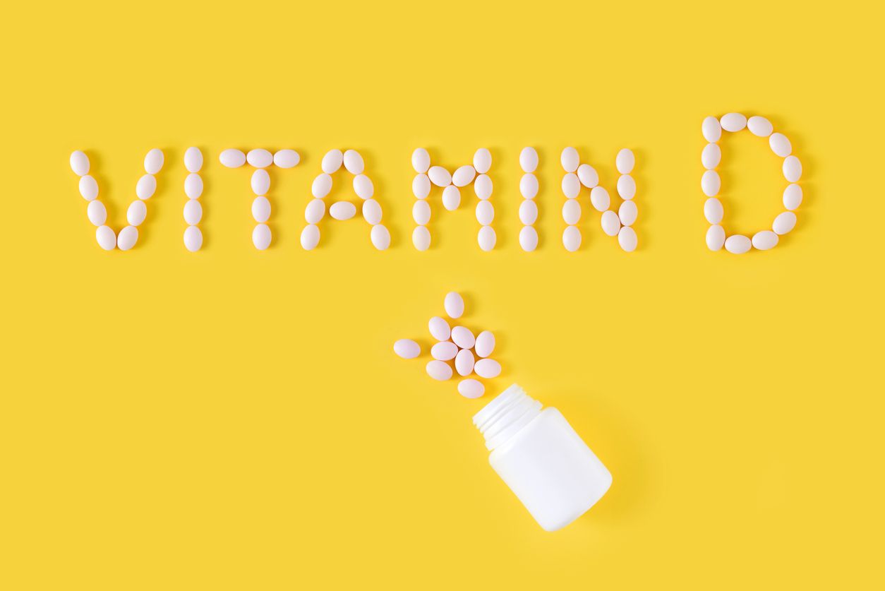Vitamin D pills dropped from bottle on yellow background. Flat lay, top view, free copy space.