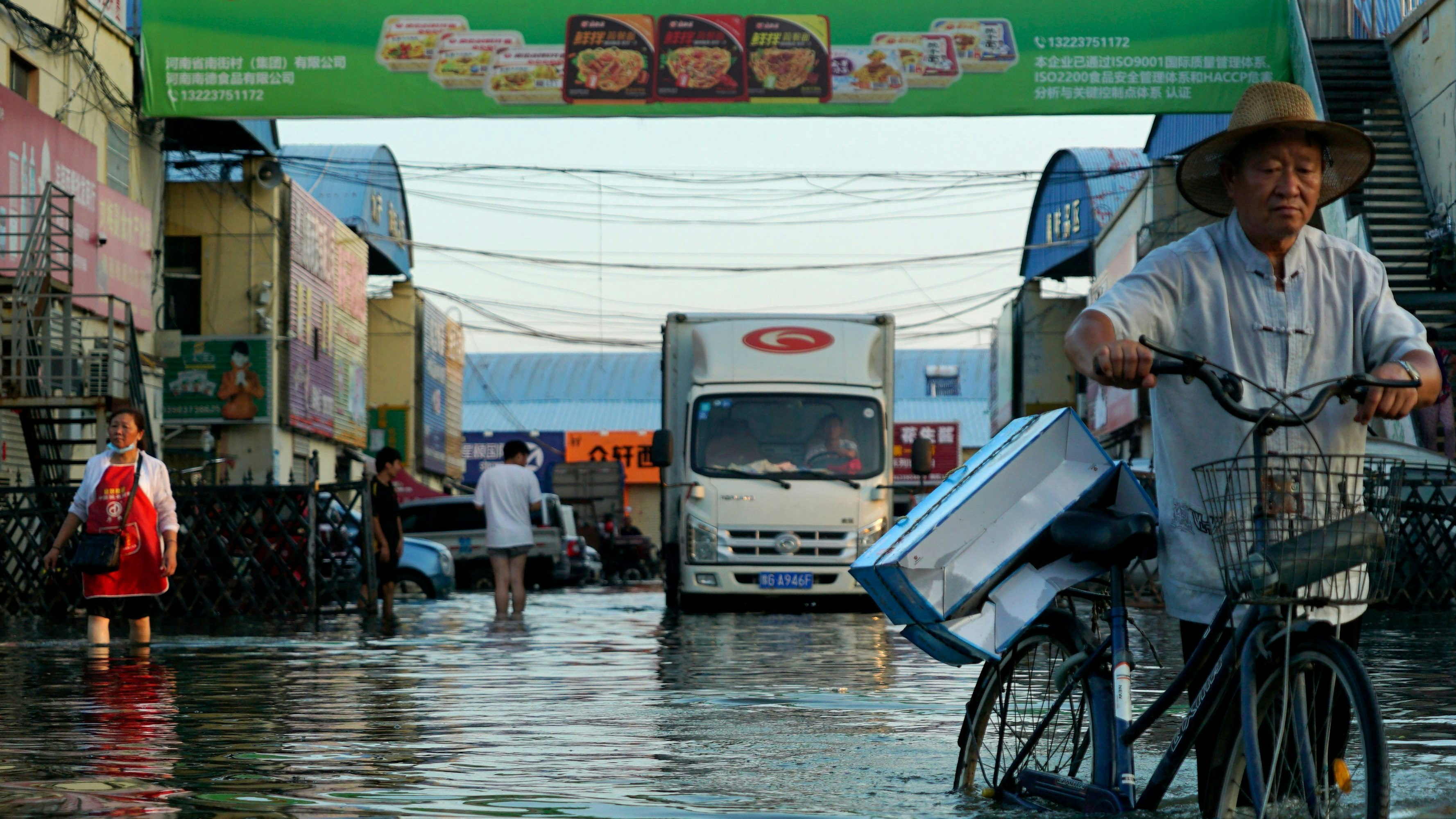 Download von www.picturedesk.com am 13.10.2021 (10:59).  FILE - In this Monday, July 26, 2021 file photo, a man carries goods on his bicycle as he walks out of the the Yubei Agricultural and Aquatic Products World in Xinxiang in central China's Henan Province. The Intergovernmental Panel on Climate Change report released on Monday, Aug. 9, 2021, says warming already is smacking Earth hard and quickly with accelerating sea level rise, shrinking ice and worsening extremes such as heat waves, droughts, floods and storms. (AP Photo/Dake Kang, File) - 20210726_PD30250 - Rechteinfo: Rights Managed (RM)