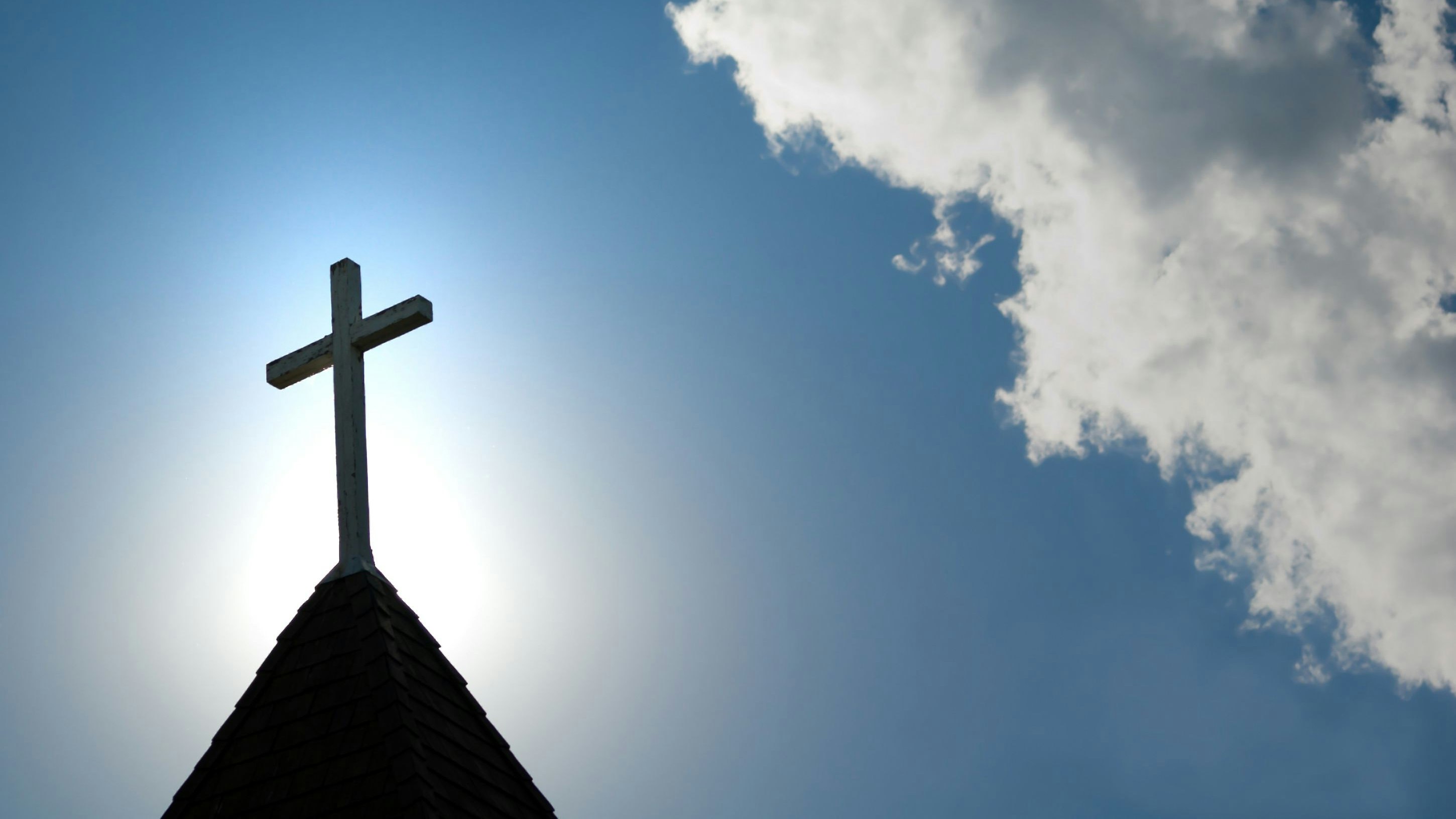 A wood cross on an old church steeple backlighted by a rising sun. Some copy space.