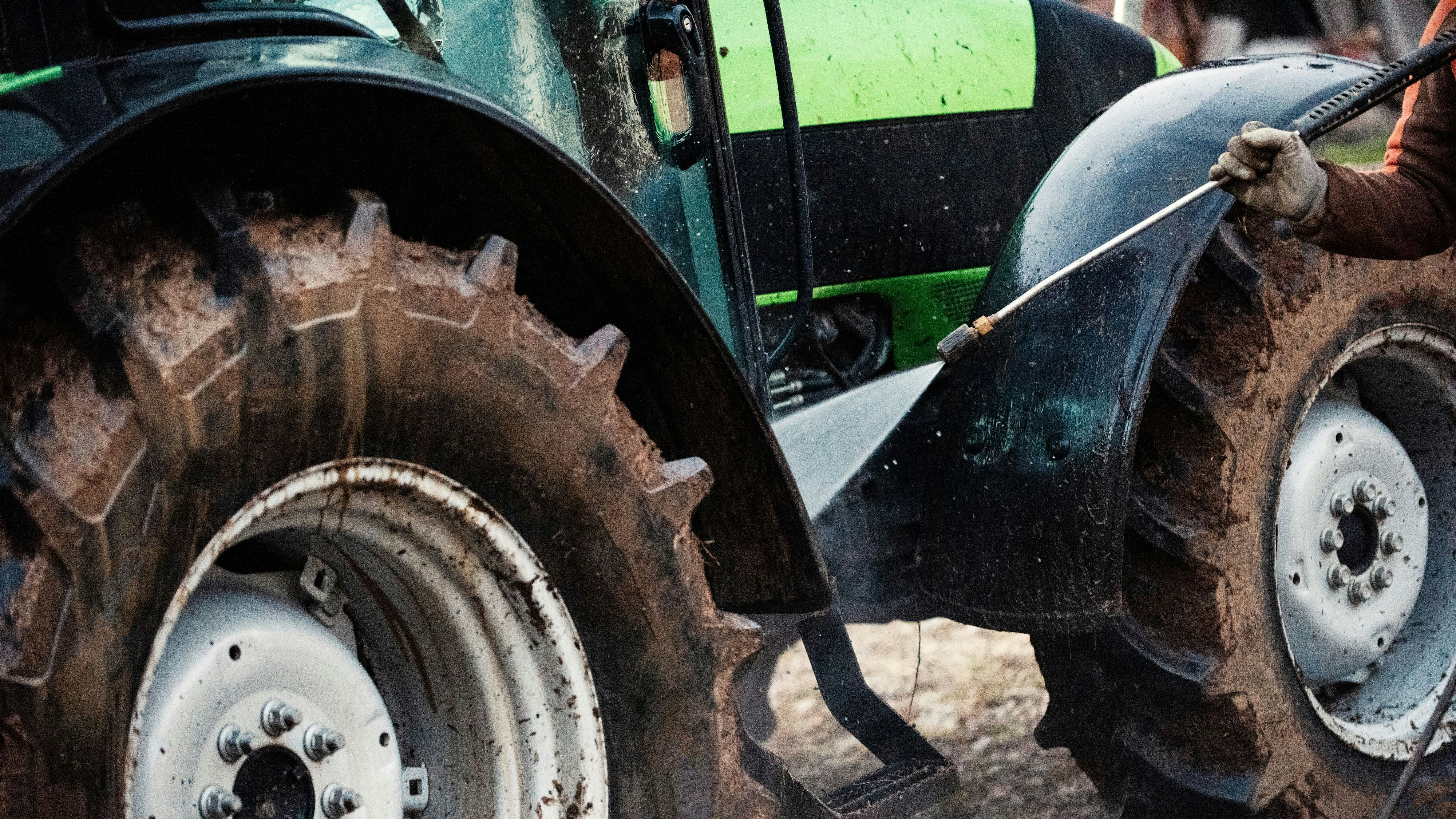 Mature man cleaning dirty tractor  with high pressure water cleaner
