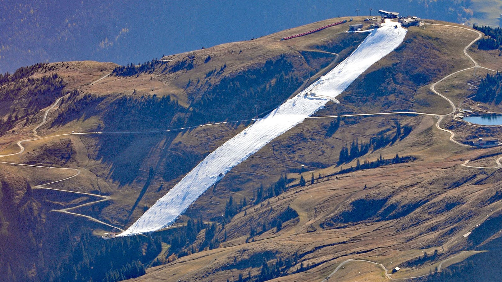 Ein weißer Streifen, inmitten sich bräunender Landschaft: So sieht das Skigebiet auf dem Resterkogel (Sbg.) zum Saisonstart aus der Luft aus.