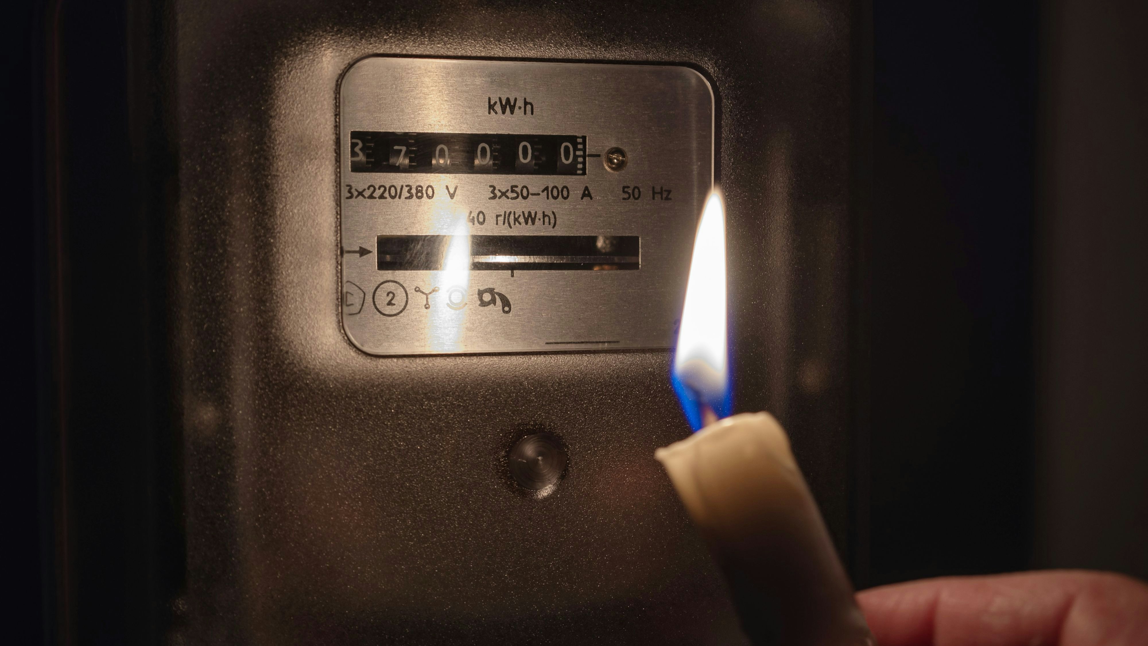 The electricity meter is illuminated by the light of a candle. Power outage, blackout concept.