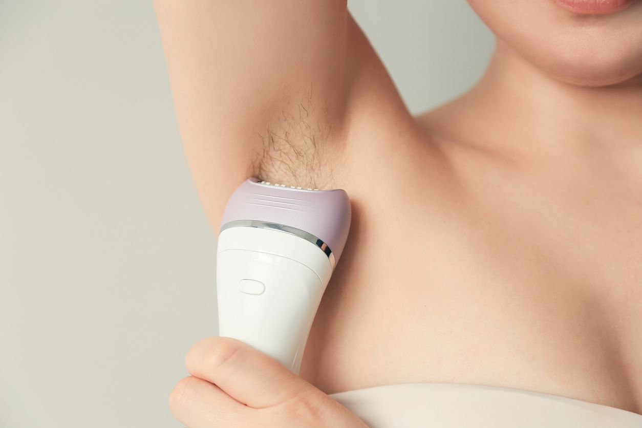 Woman takes care of herself, depilated armpits with an epilator. Epilation Cosmetology procedure for hair removal. SPA concept.