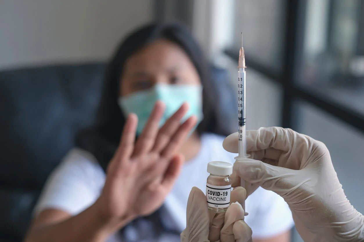 Close-up shot of an unrecognizable doctor holding a syringe and covid-19 vaccine in front of a Malaysian woman who refusing the Covid-19 vaccine.