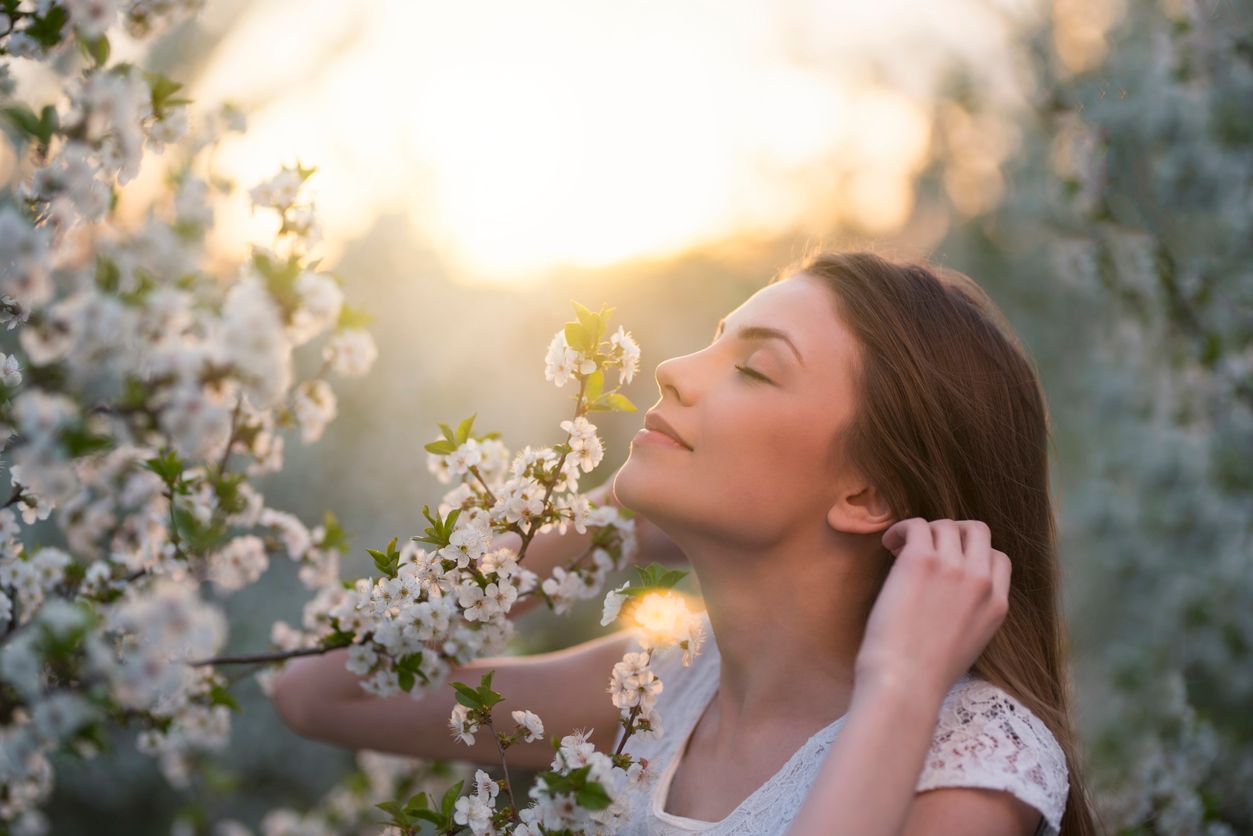 Beautiful, young woman among trees in bloom, enjoying the smell of flowers with her eyes closed.