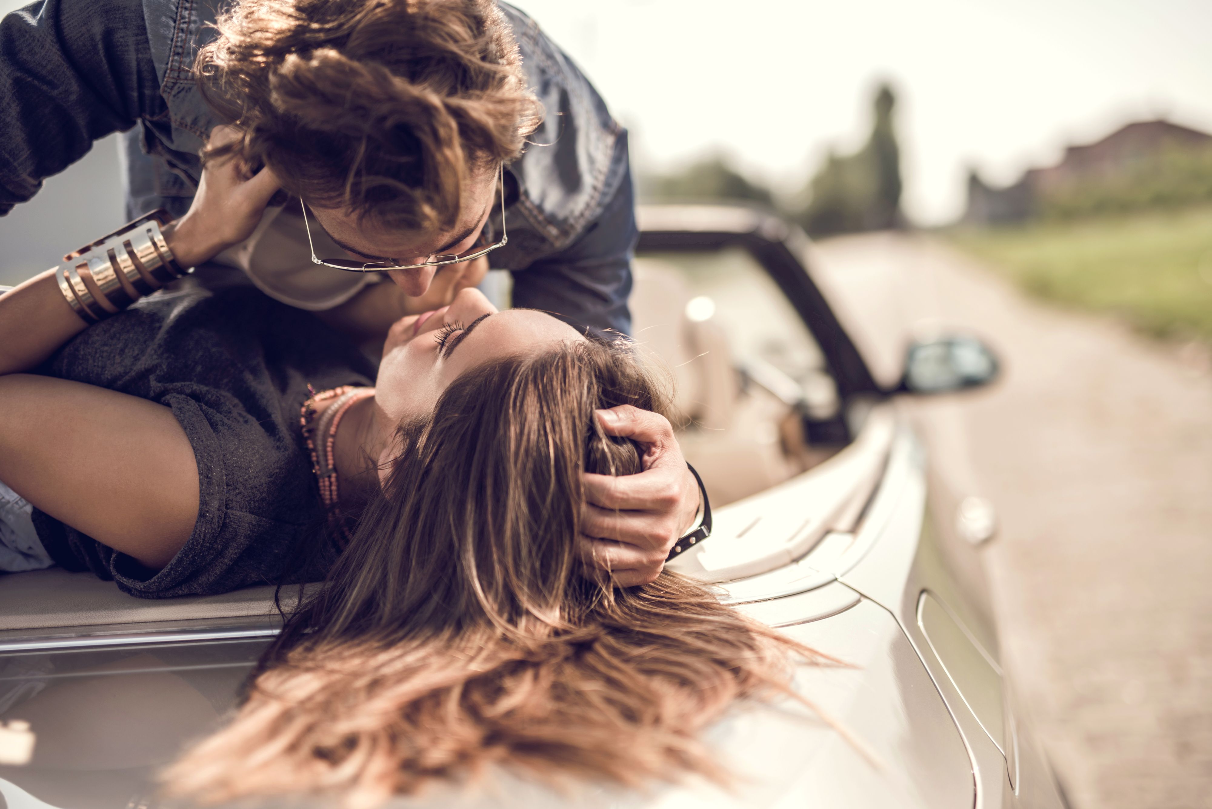 Young loving couple having a desire toward each other while lying on cabriolet.