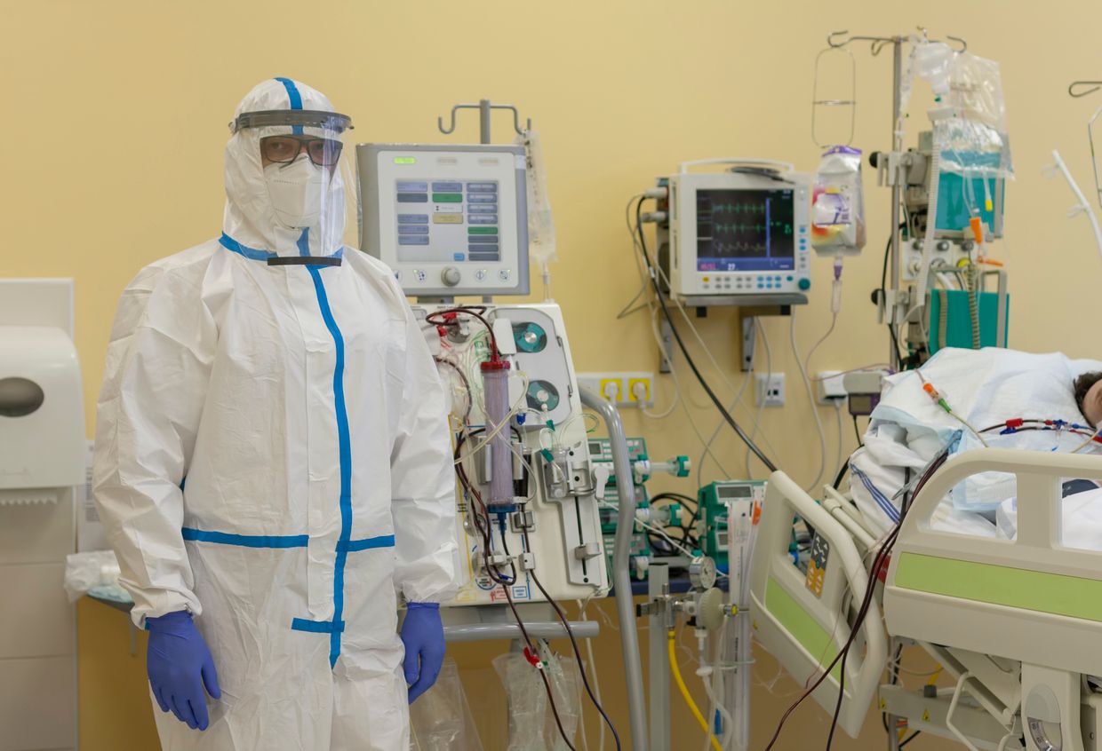 Male nurse with protective coverall clothing in intensive care unit in hospital.  Dialysis machine, to which patient is connected.  The patient fell ill with a new type of coronavirus covid-19.
