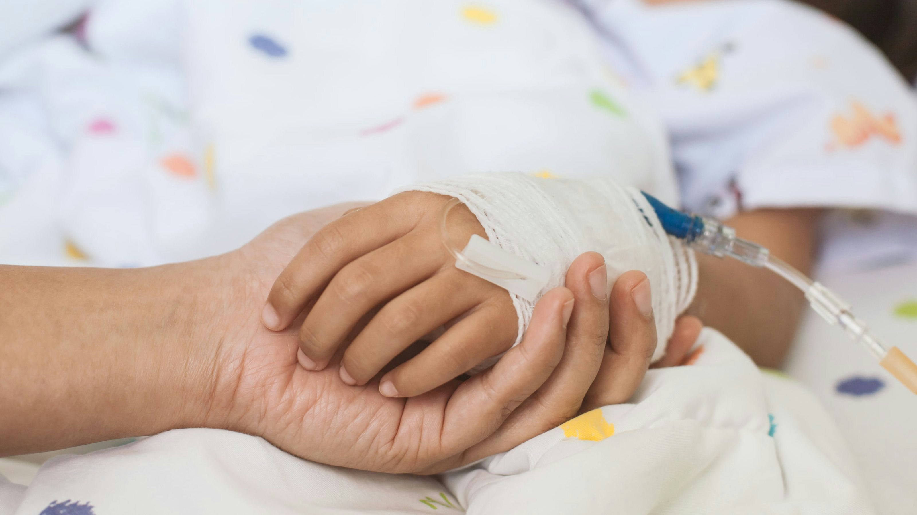 Mother hand holding sick daughter hand who have IV solution bandaged with love and care while she is sleeping on bed in the hospital