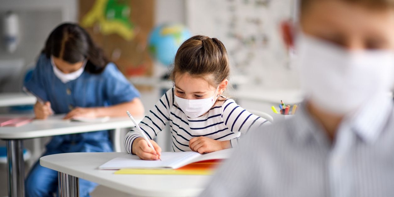 Small children with face mask back at school after covid-19 quarantine and lockdown, writing.