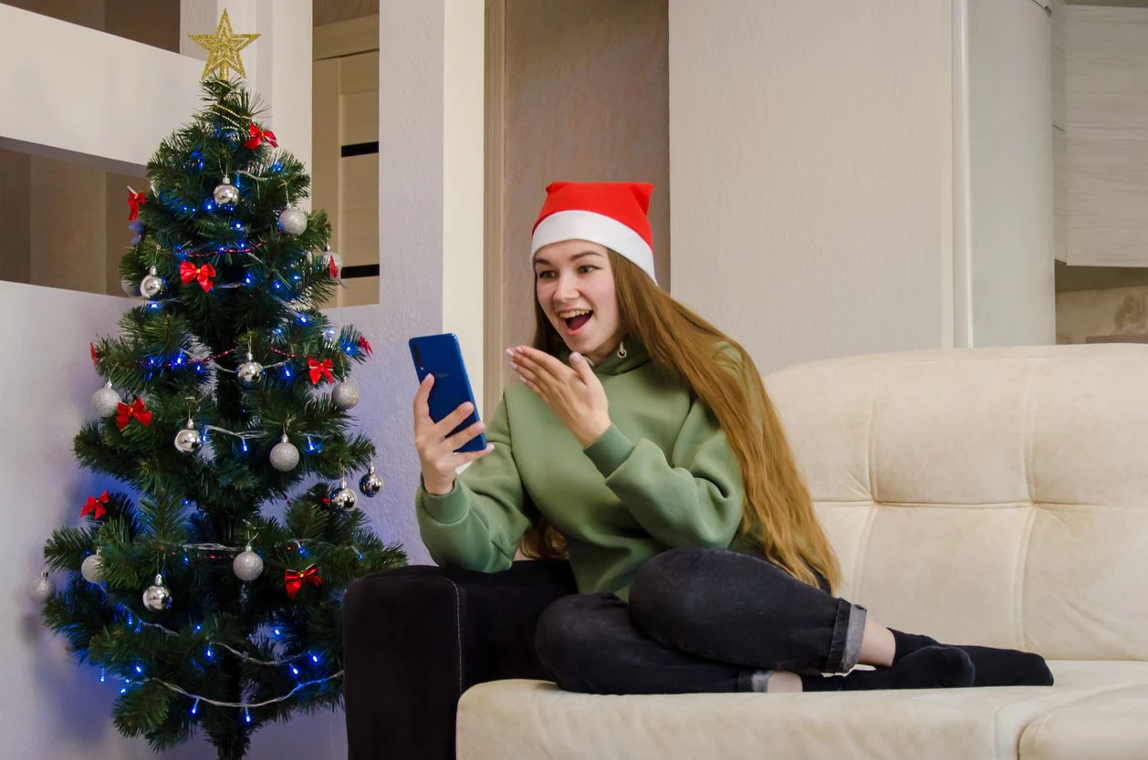 the girl sits near the Christmas tree and looks at the phone and is surprised by the message. surprise. High quality photo