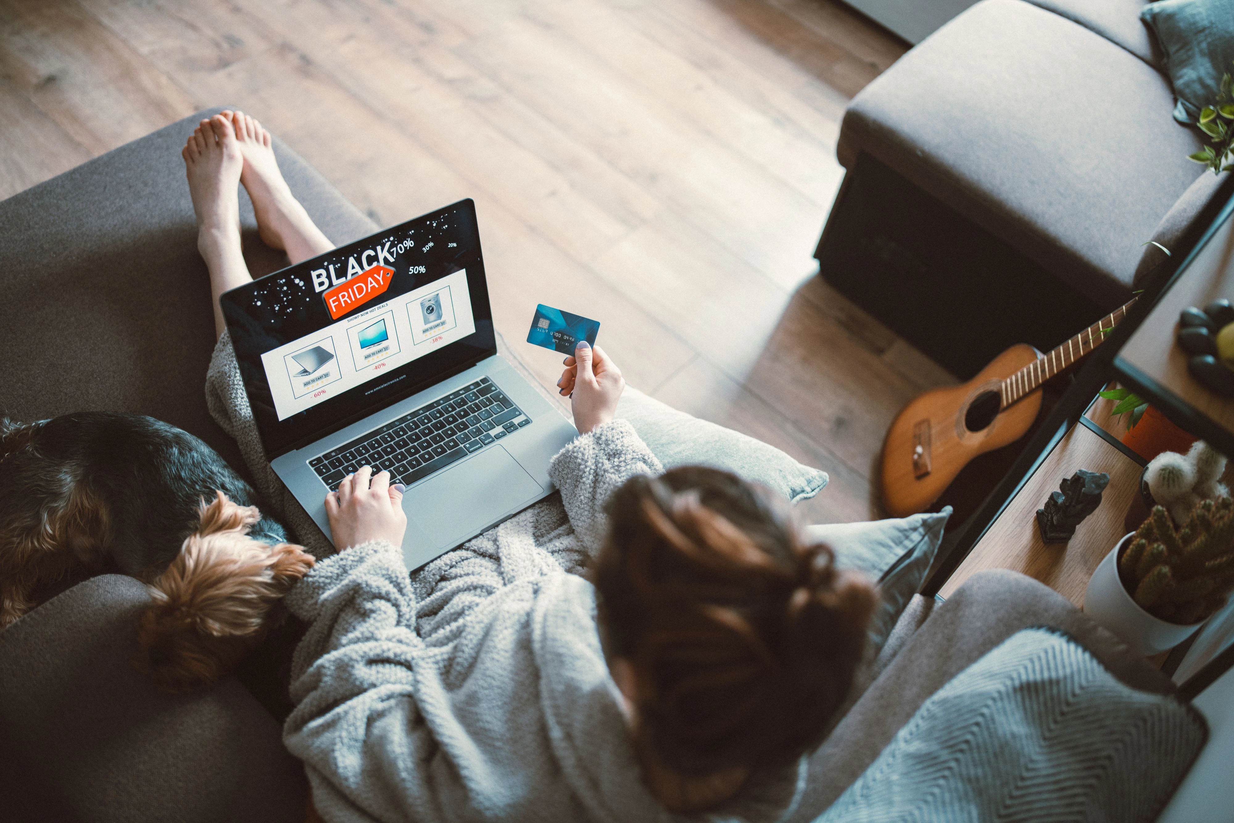 Woman relaxing on sofa at home and shopping online at Black Friday event and her dog sleeping around.