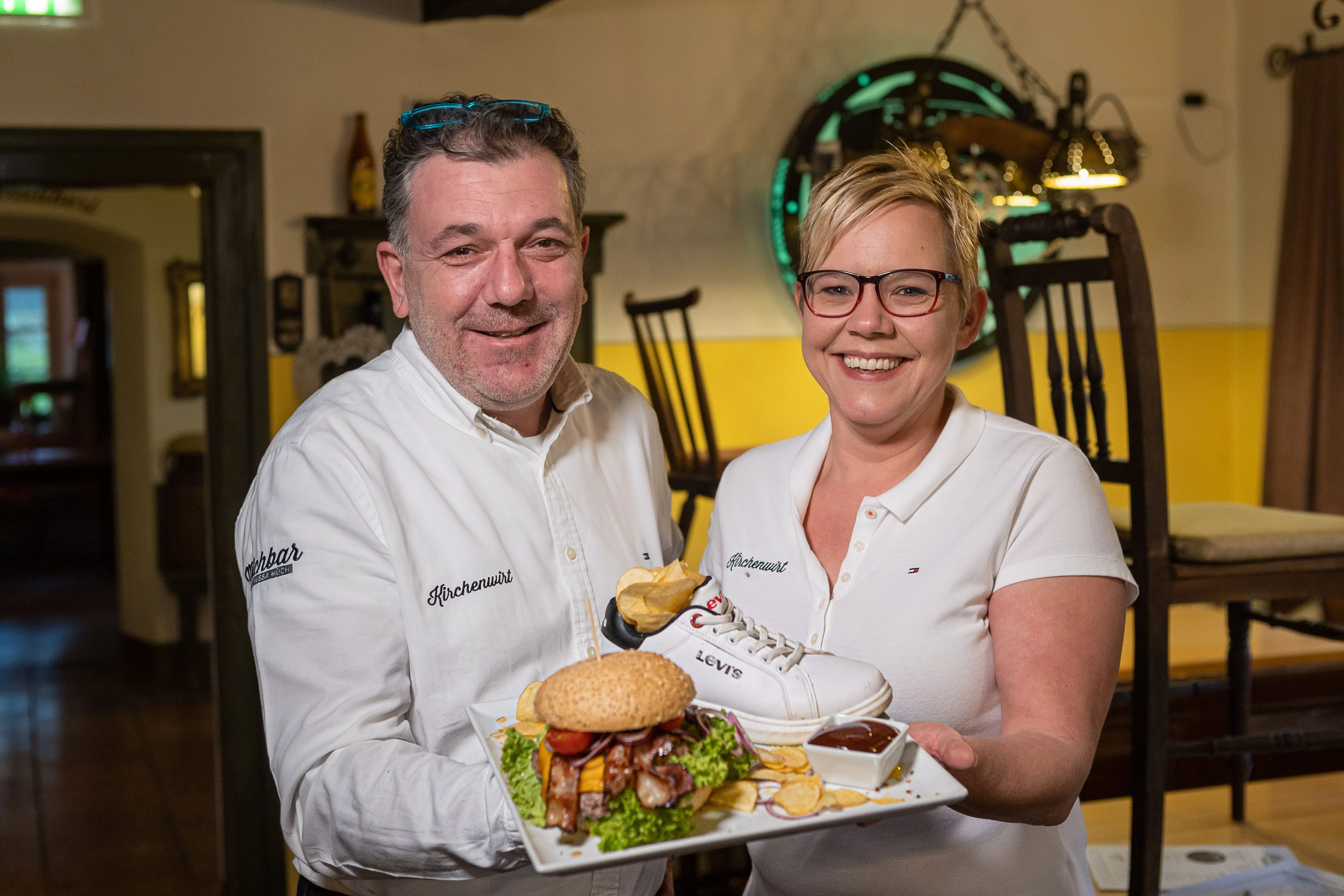 Beim Kirchenwirt in Perwang gibt es eine eigene Lockdown-Speisekarte 26.11.2021 Foto: Chris Hofer Bild zeigt: Mario Mairhofer mit Mitarbeiterin Alexandra Mieser und ein Mückstein-Burger - Pommes im Turnschuh serviert
