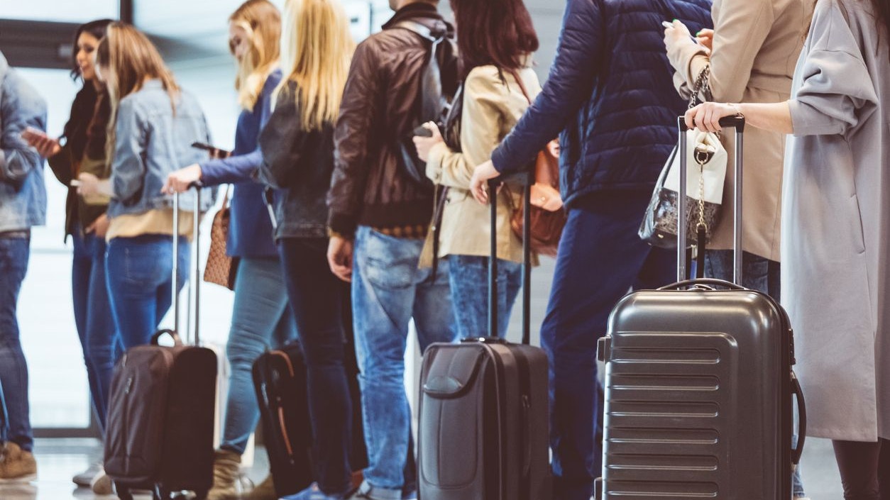 Shot of queue of passengers waiting at boarding gate at airport. Group of people standing in queue to board airplane.