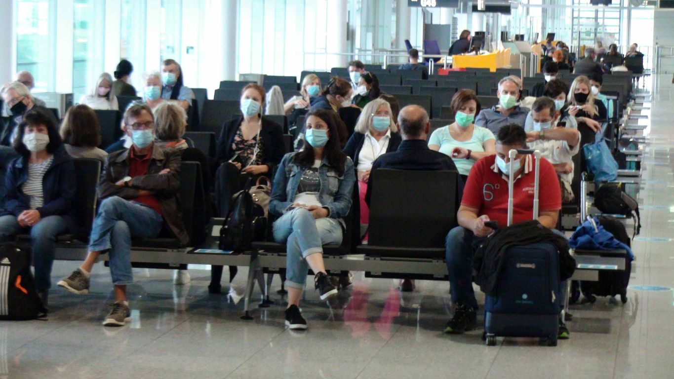 Scene Of People Sitting Down, Standing, Looking Around, Talking To One Another, Wearing Face Mask Due To Coronavirus Pandemic, Getting Ready To Board Passengers Airplane At Munich International Airport In Bavaria Germany Europe
