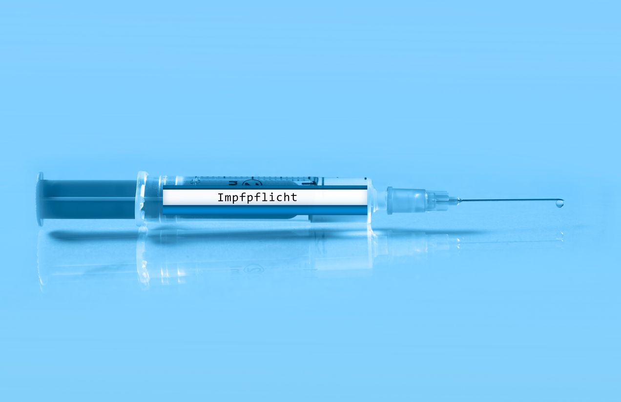 close up of a syringe with the german inscription vaccination obligation on a light blue background