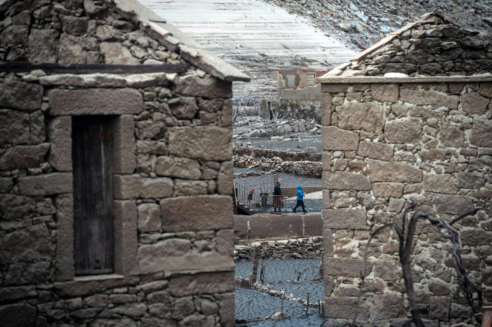 Wanderer erkunden die Ruinen, viele Steinmauern stehen noch, bei einigen Häusern sind gar nur die Dächer eingestürzt.