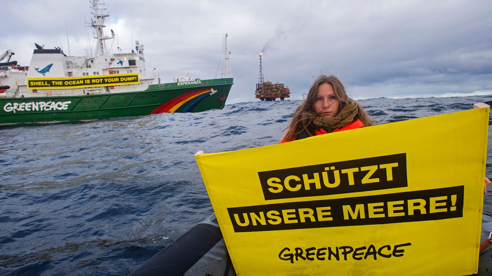 Die Greenpeace-Aktivistin Jennifer Ganster hält ein Banner mit der Aufschrift "Schützt unsere Meere" bei einer Demonstration gegen Shell im Brent-Feld. Das Greenpeace-Schiff Esperanza fährt vor der von Shell betriebenen Ölplattform Brent-C (Charlie) im Hintergrund vorbei. Die Anlage befindet sich im Ölfeld Brent im britischen Teil der Nordsee.