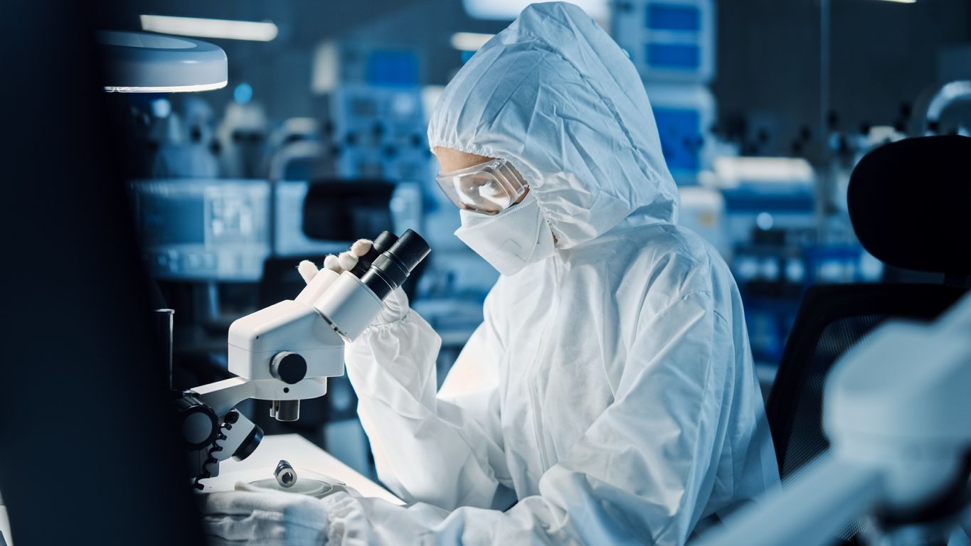 Research Factory Cleanroom: Engineer / Scientist wearing Coverall and Gloves Uses Microscope to Inspect Motherboard Microprocessor Components, Developing High Tech Modern Electronics