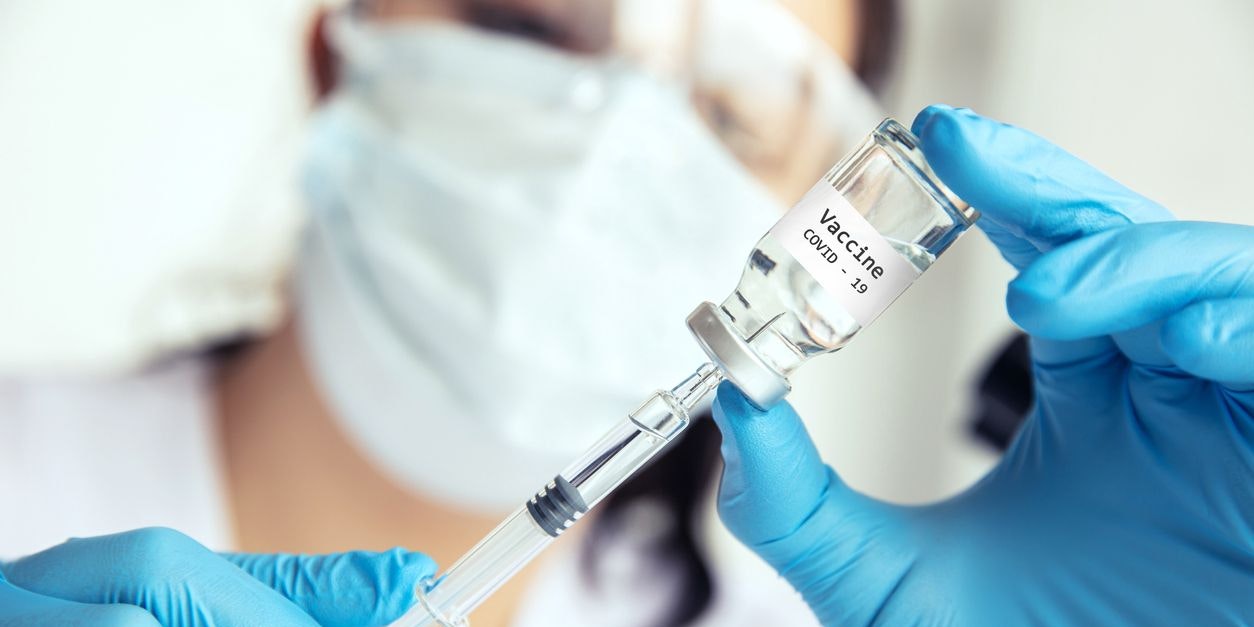 Scientist draws medicine into the syringe. Female scientist in protective mask, glasses and gloves draws Covid-19 vaccine into the syringe.