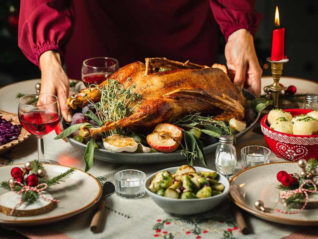 Close-up of woman's hands setting the table, serving roast duck for Christmas dinner.