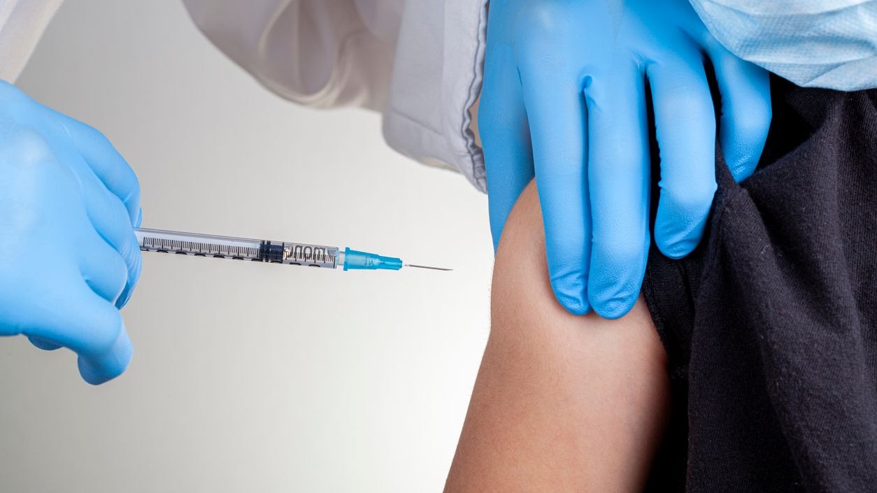 A health care professional wearing gloves and white coat is administering a childhood vaccine to a caucasian kid. Closeup Concept image for child vaccination, immunization clinical trial