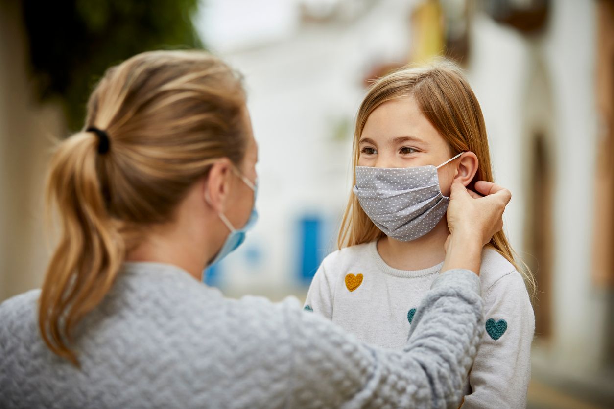 A mother wearing surgical mask helps daughter putting home made face mask during coronavirus pandemic.