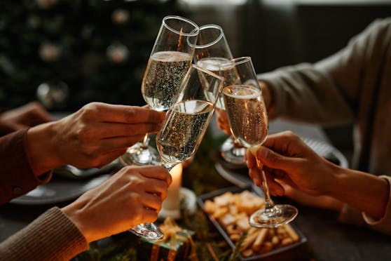 Close up of four people enjoying Christmas dinner together and toasting with champagne glasses while sitting by elegant dining table with candles