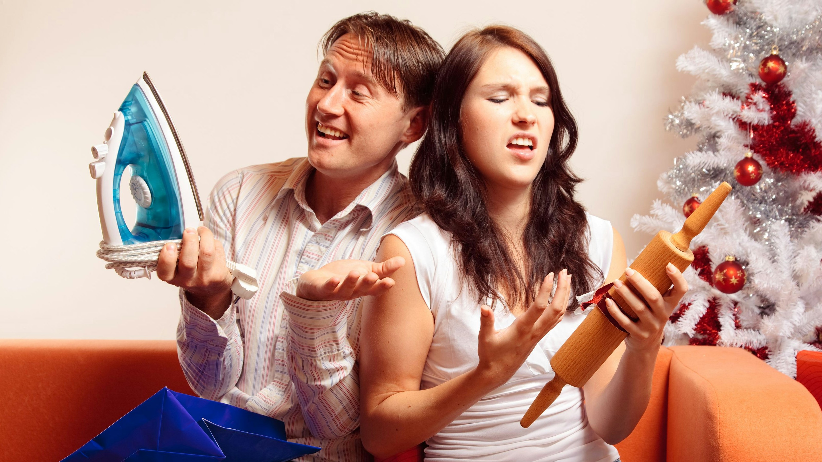 a young couple is sitting on the couch and exchanging christmas gifts. both of them seem quite unhappy with the stuff they got....