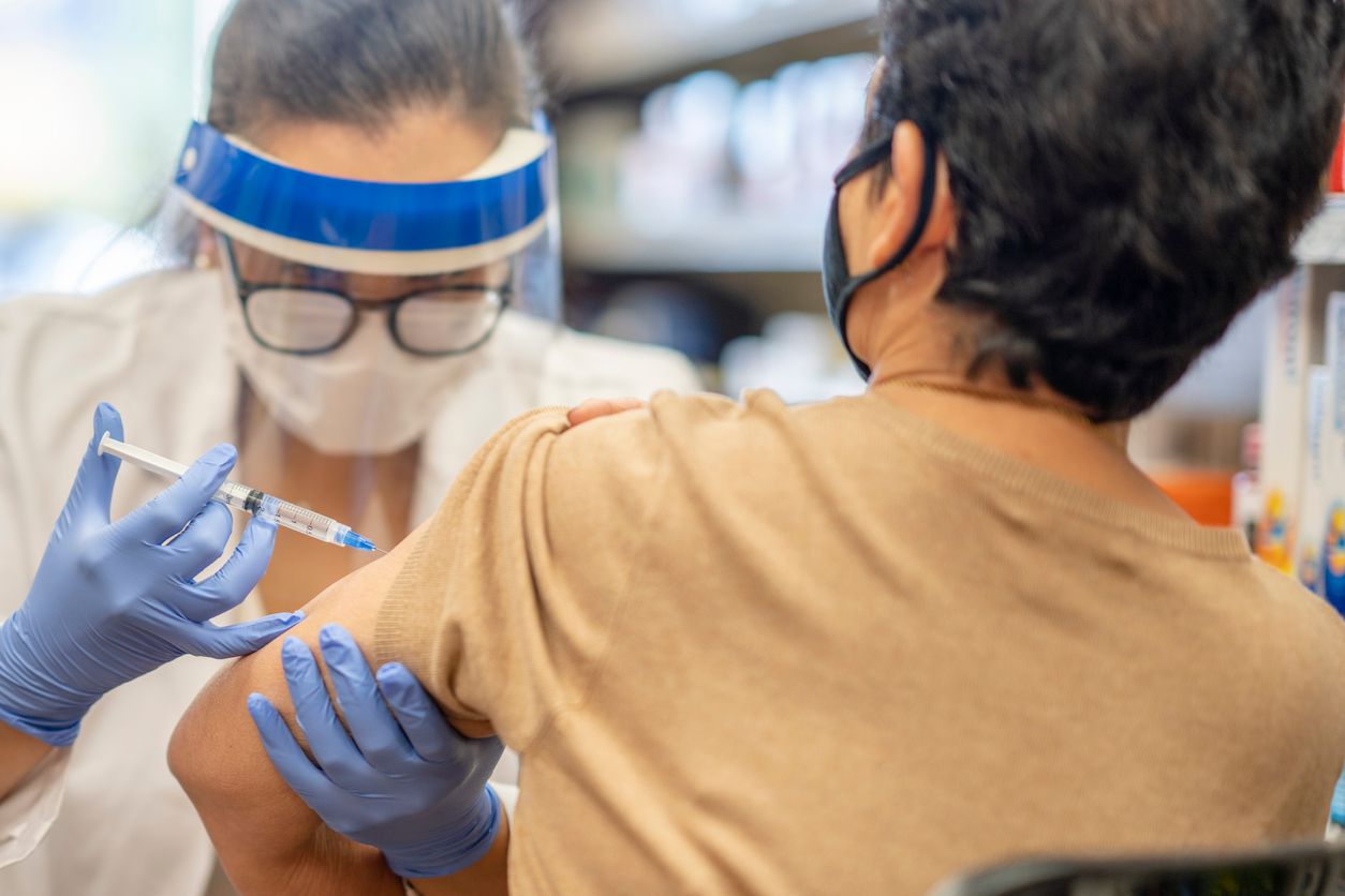 Masked senior woman getting a vaccine while at the pharmacy by a female pharmacist.