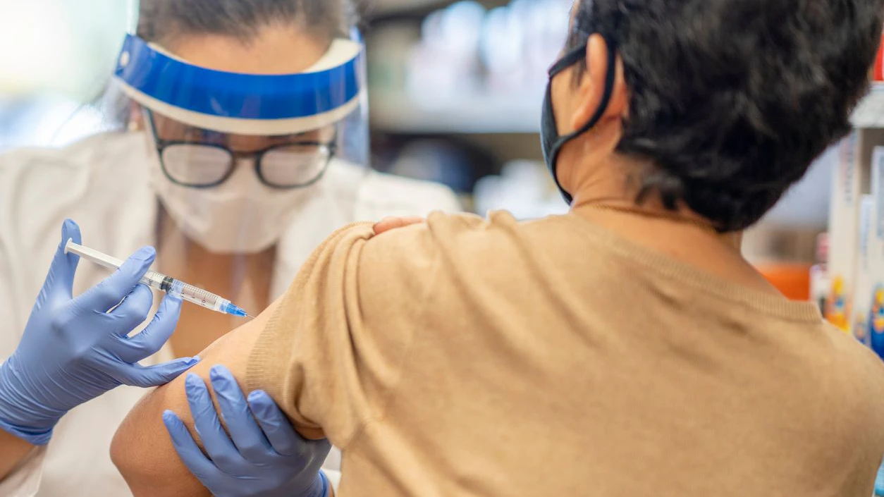 Masked senior woman getting a vaccine while at the pharmacy by a female pharmacist.