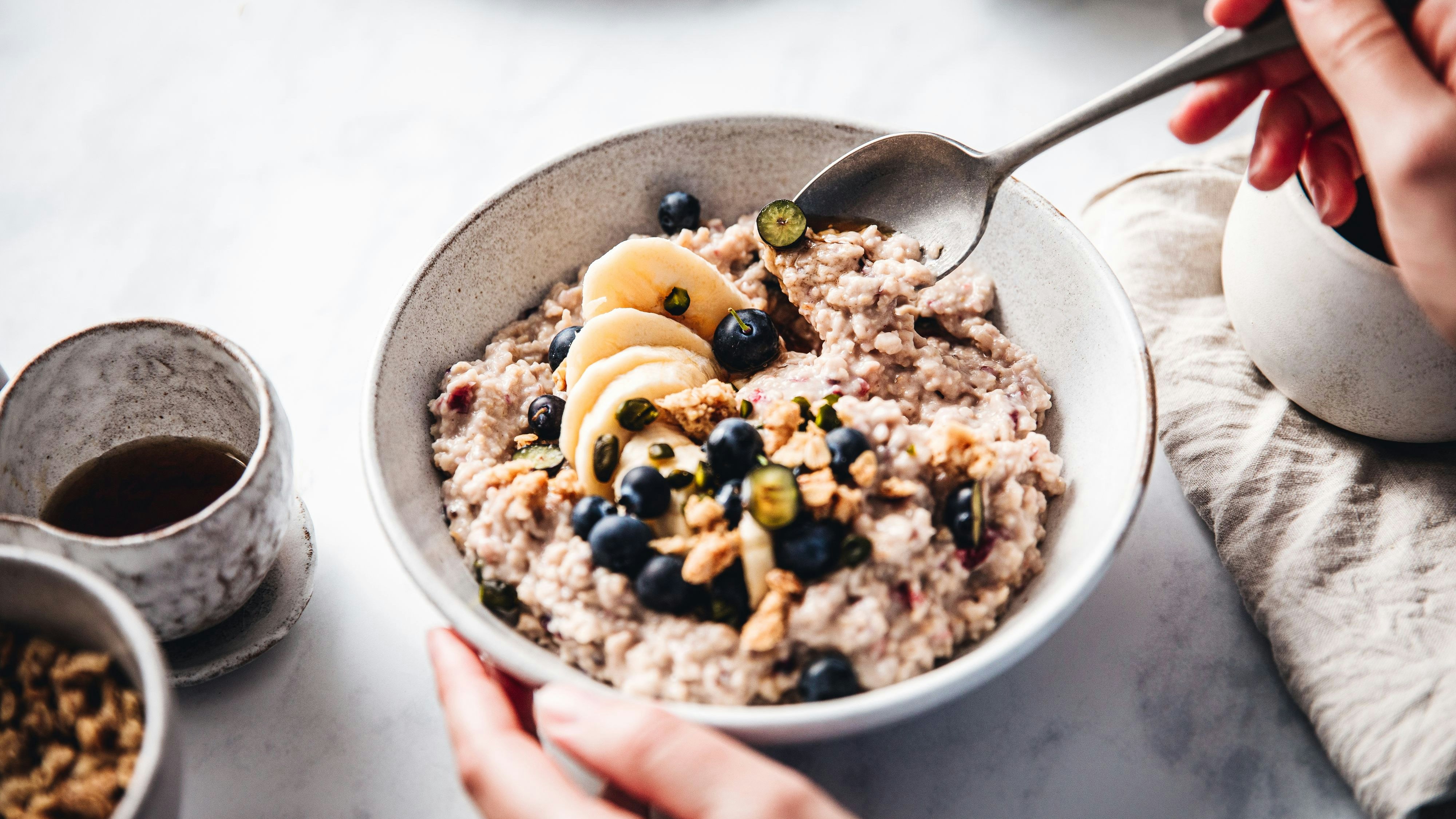 Close-up of a woman mixing oats flour, banana and blueberries in a bowl. Female making healthy breakfast in kitchen.