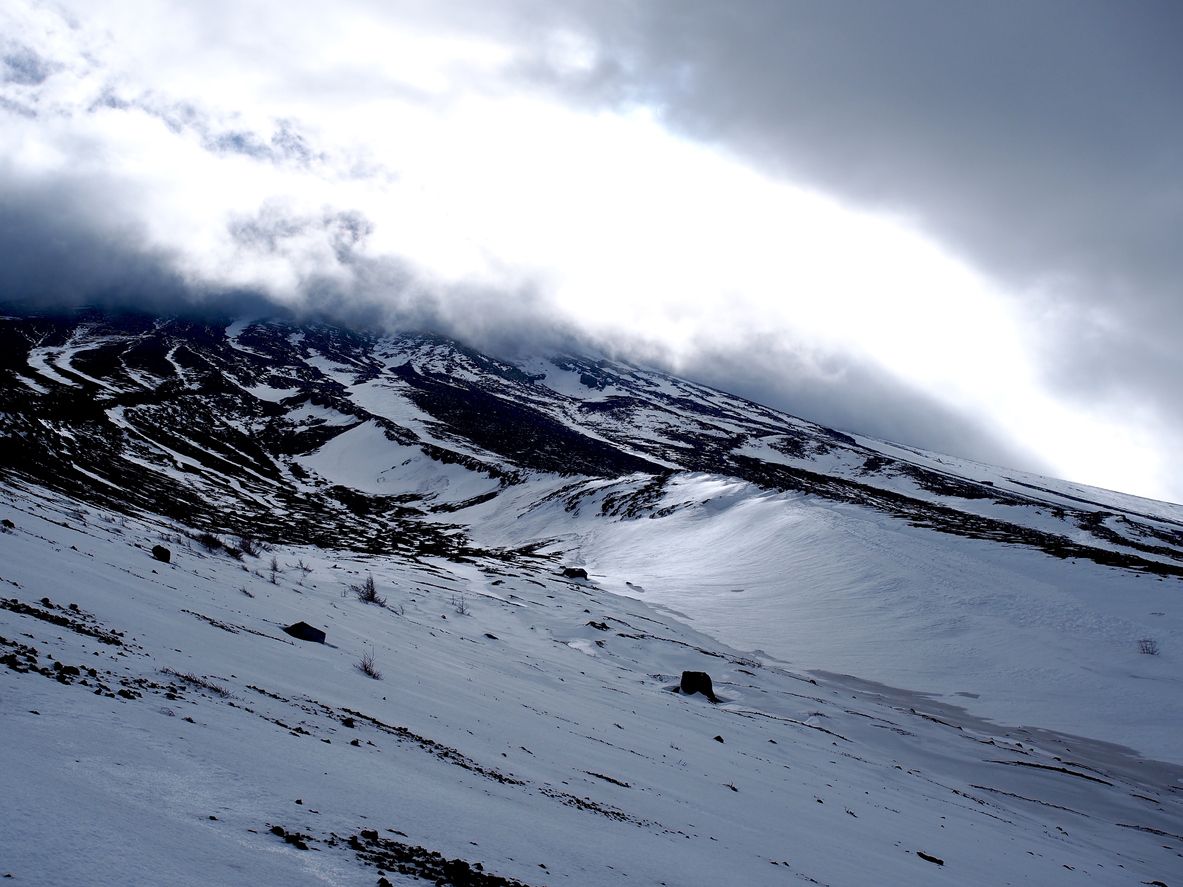 Mt. Fuji being covered with snow. The sun manages to break through the heavy clouds, reflecting off the white ice.