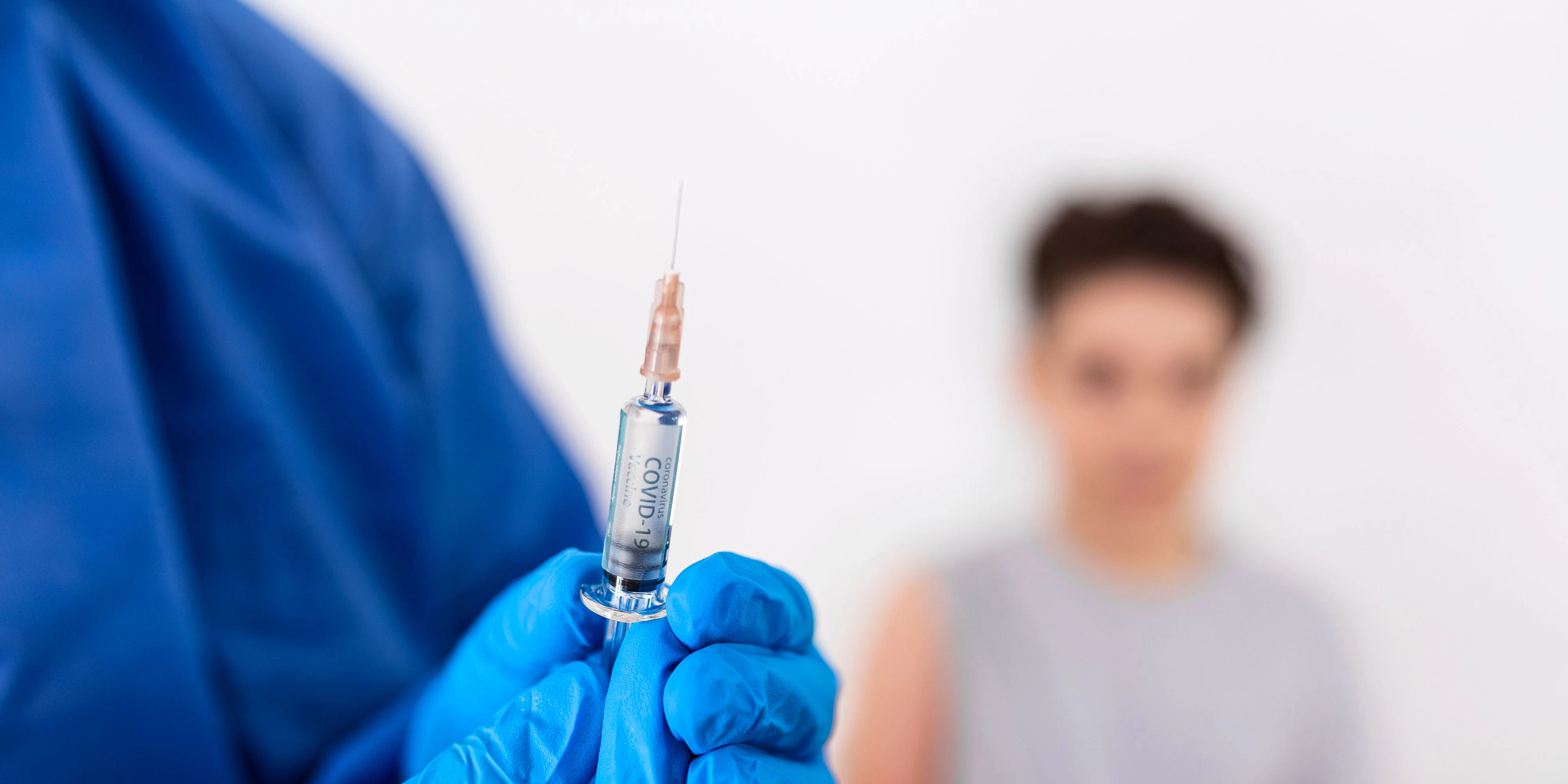 Vaccination. Professional doctor in blue sterile gloves holding syringe and making injection to a little boy wearing medical mask. Immunisation, medicine and healthcare. Covid19, coronavirus vaccine