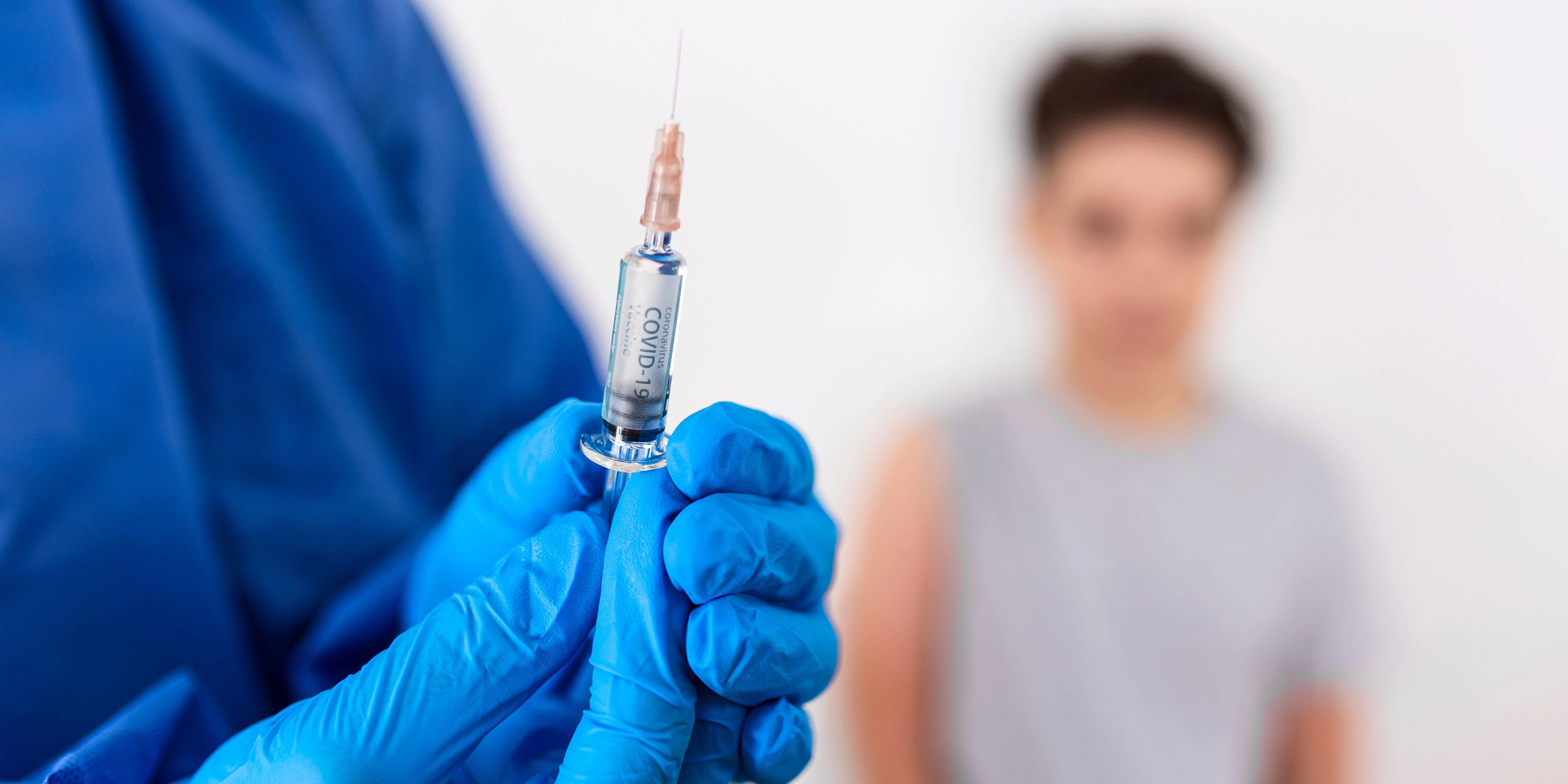 Vaccination. Professional doctor in blue sterile gloves holding syringe and making injection to a little boy wearing medical mask. Immunisation, medicine and healthcare. Covid19, coronavirus vaccine