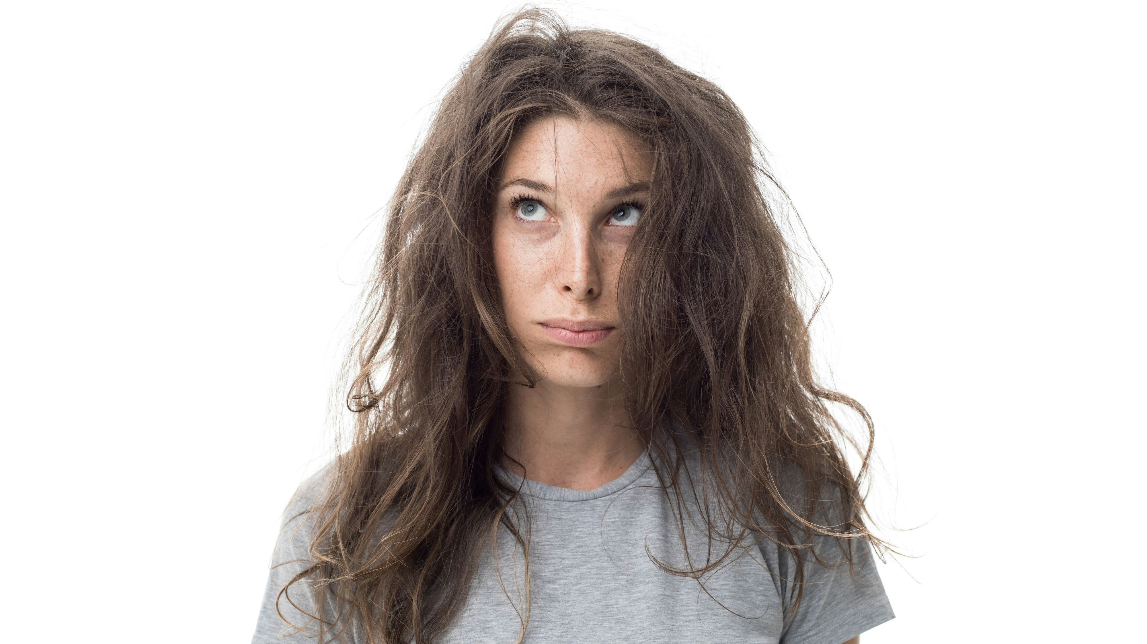 Angry young woman having a bad hair day, her long hair is messy and tangled