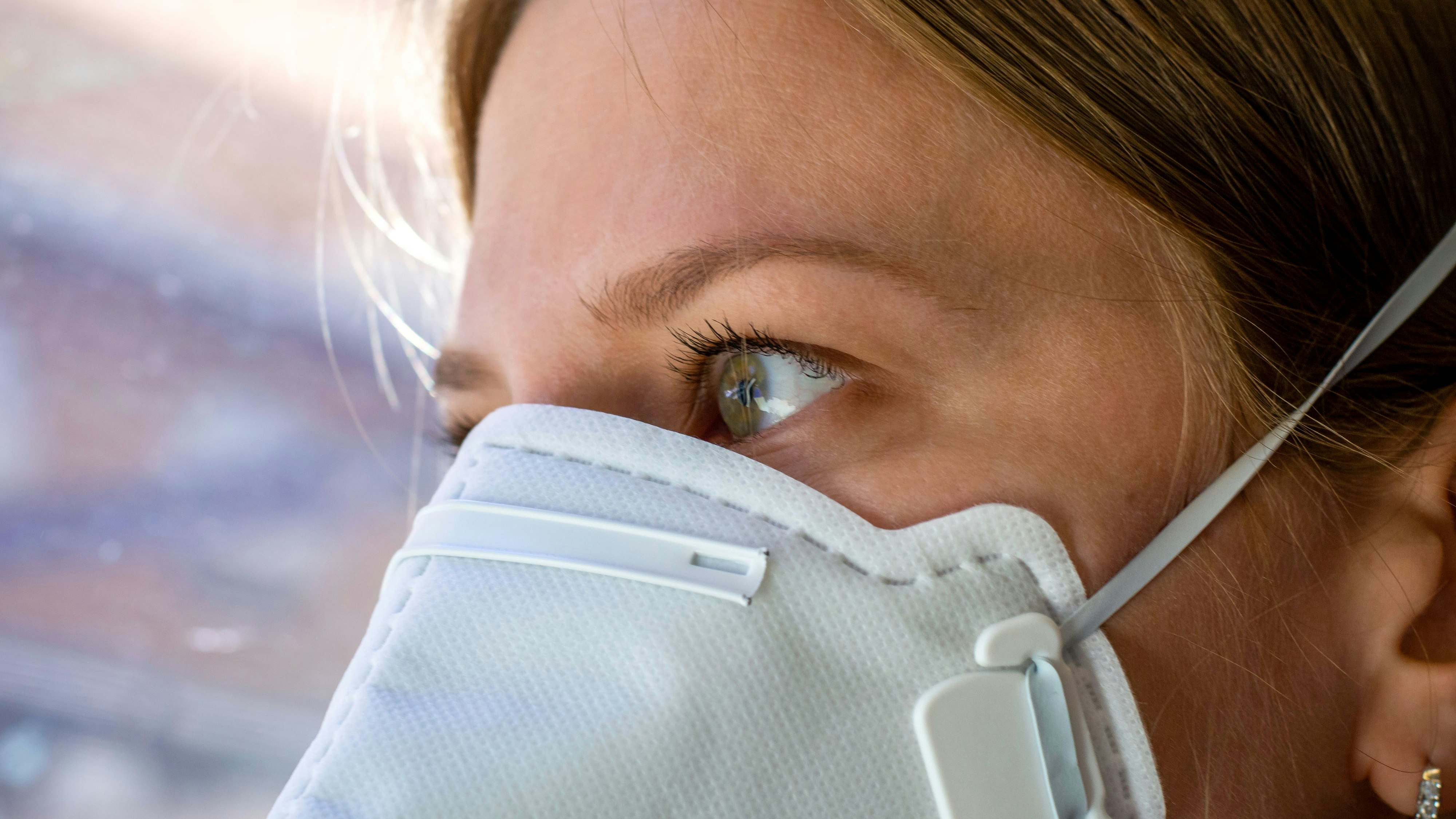 Close up woman wearing a FFP3 face mask looking outside. Disposable respirator protective mouth filter mask. Concept of covid-19 coronavirus.