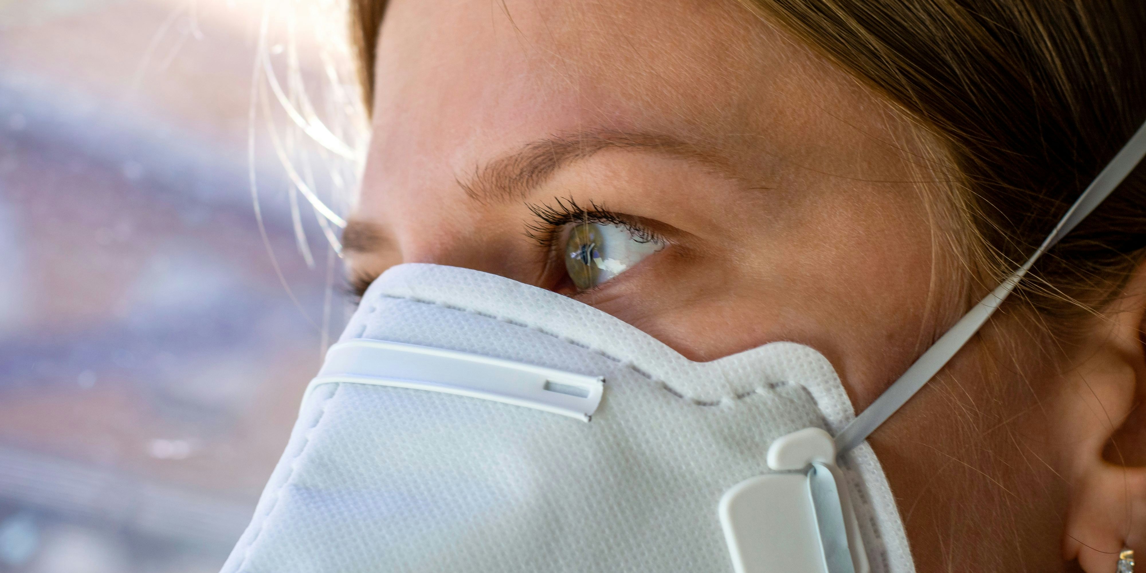 Close up woman wearing a FFP3 face mask looking outside. Disposable respirator protective mouth filter mask. Concept of covid-19 coronavirus.