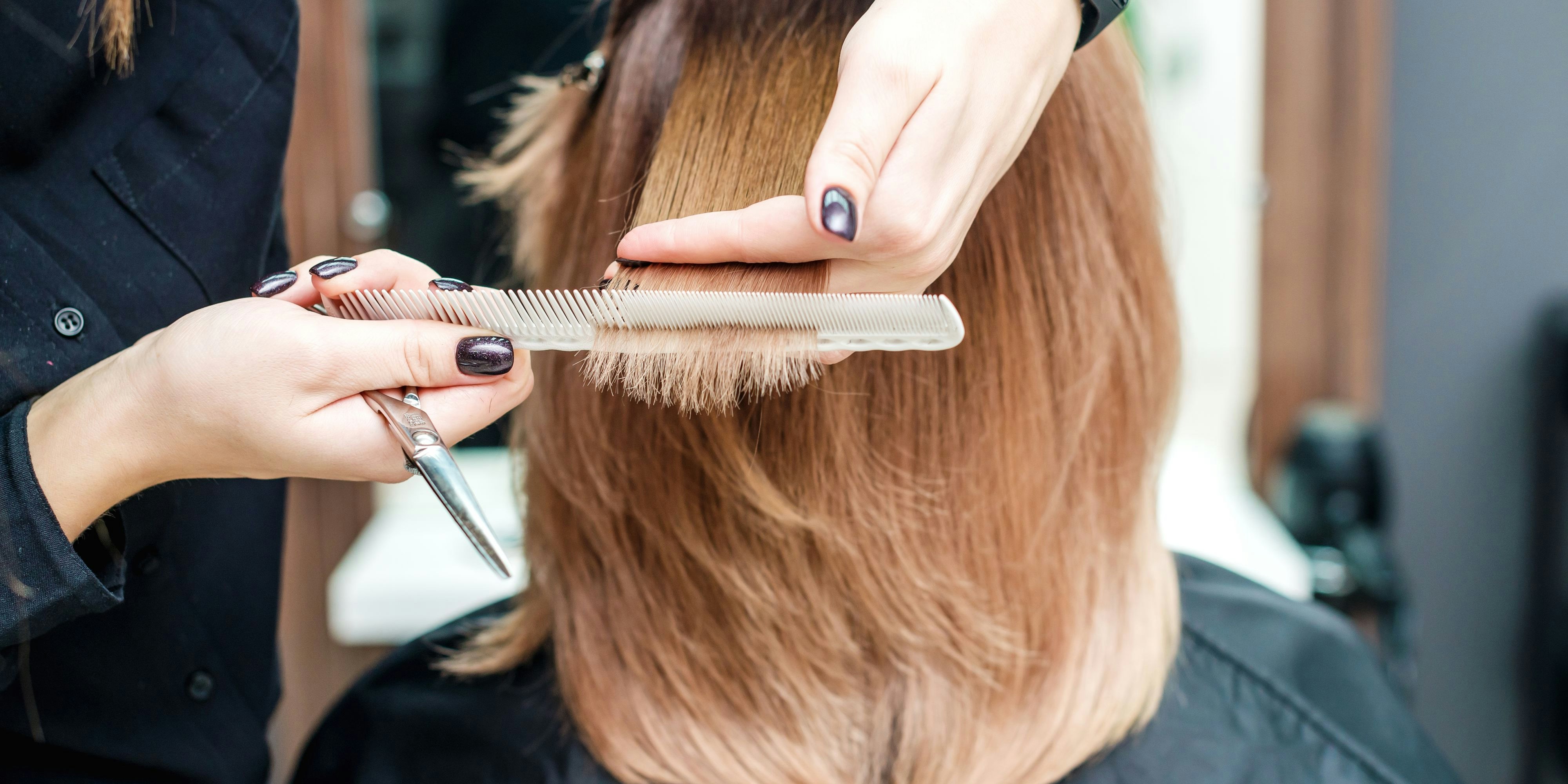Hairdresser's female hands are holding woman's red hair with comb between fingers in the beauty salon close up.