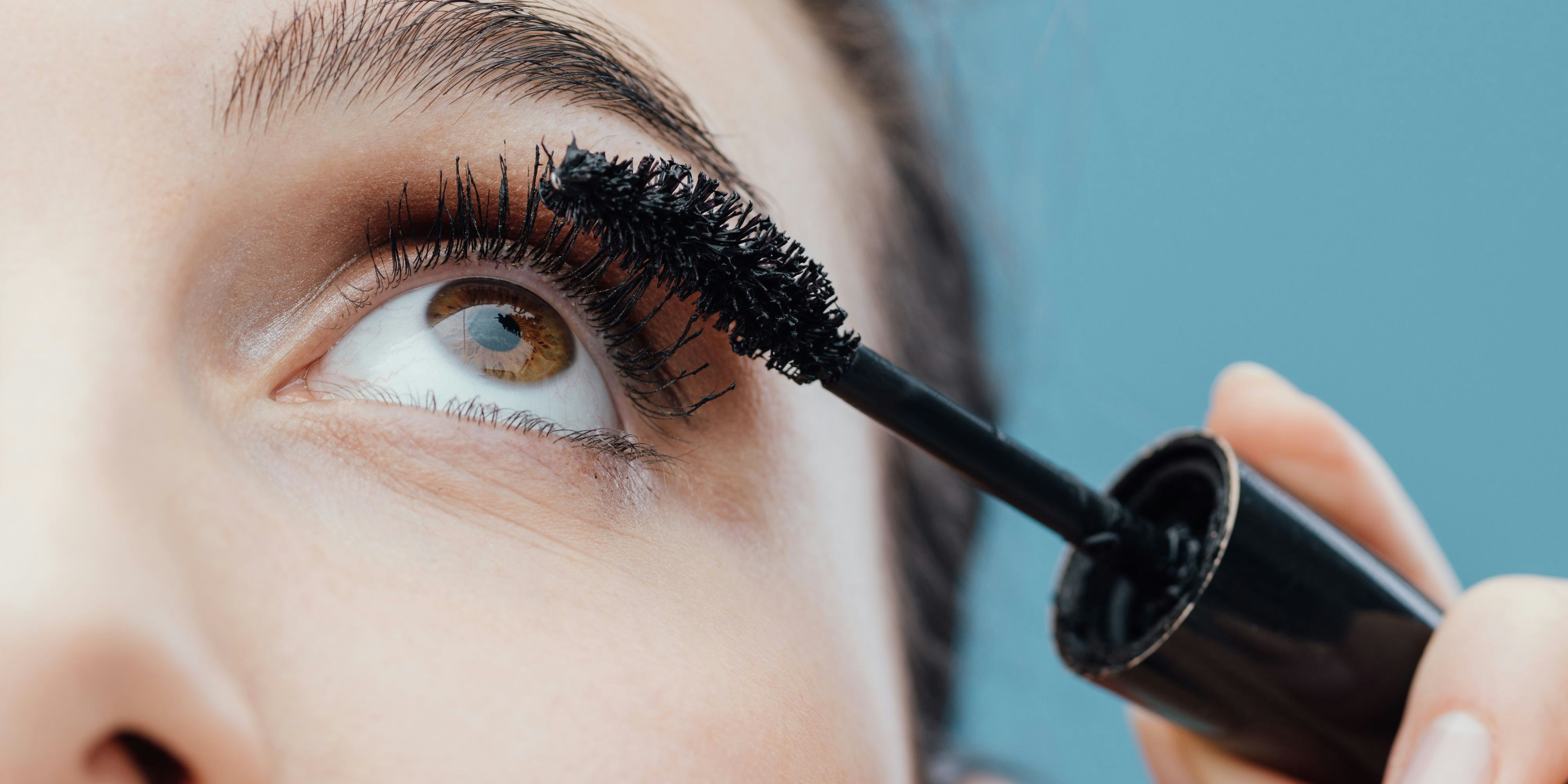 Woman applying mascara on her lashes, make up and cosmetics concept