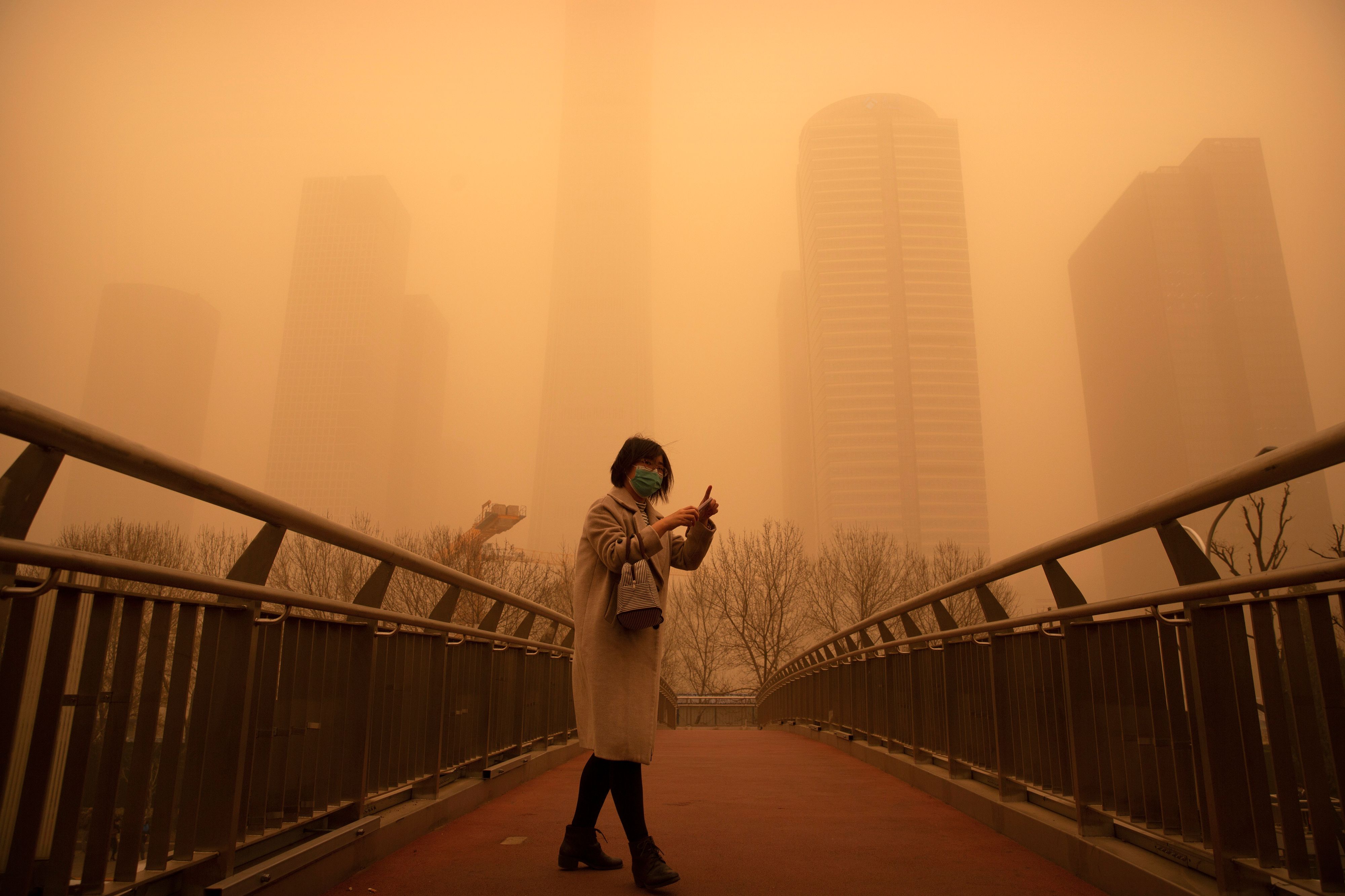 Download von www.picturedesk.com am 15.03.2021 (12:45).  A woman walks along a pedestrian bridge amid a sandstorm during the morning rush hour in the central business district in Beijing, Monday, March 15, 2021. The sandstorm brought a tinted haze to Beijing's skies and sent air quality indices soaring on Monday. (AP Photo/Mark Schiefelbein) - 20210315_PD0328 - Rechteinfo: Rights Managed (RM)