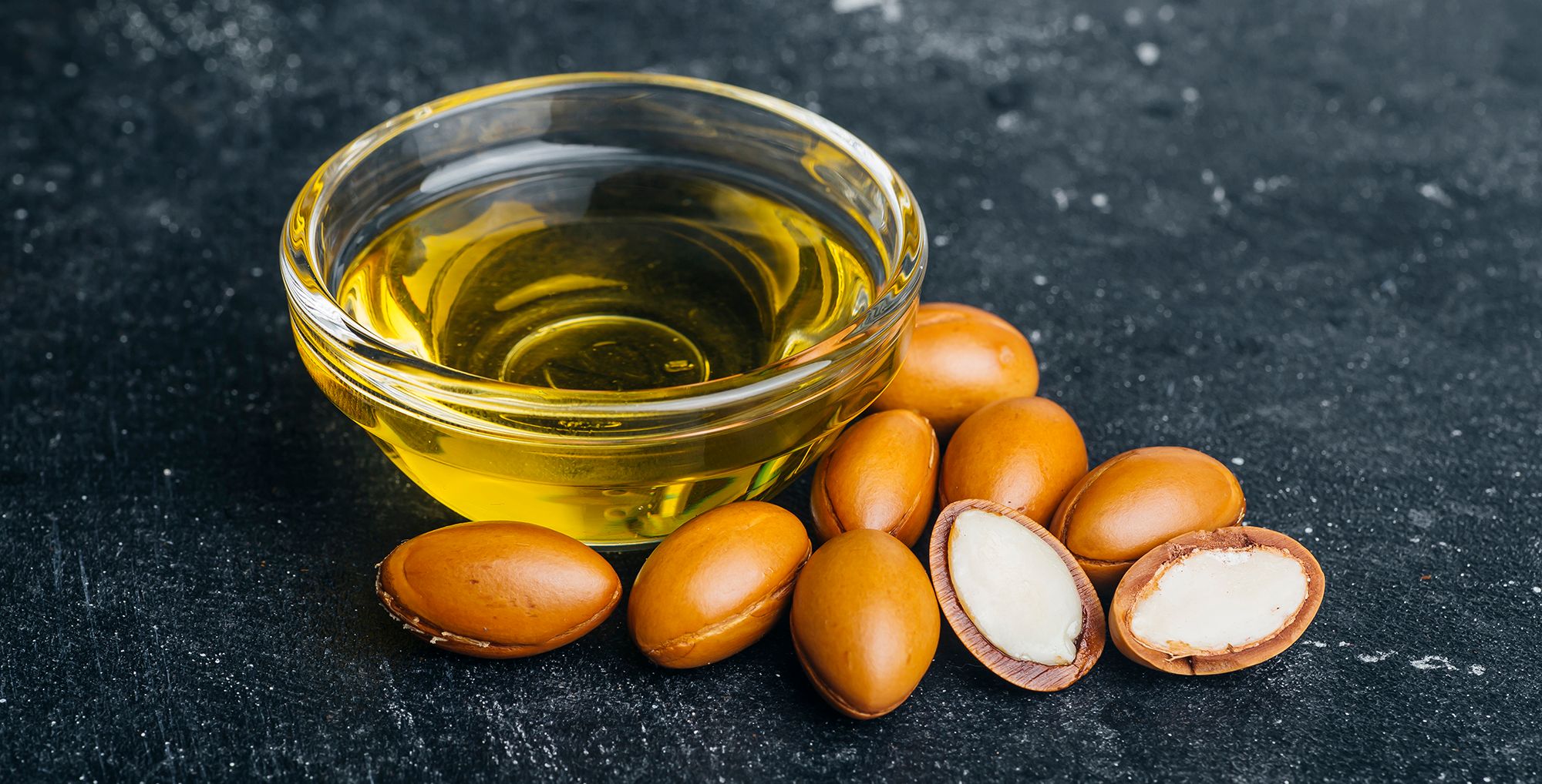 Argan seeds and oil on a dark wooden background. Argan oil based cosmetics concept.