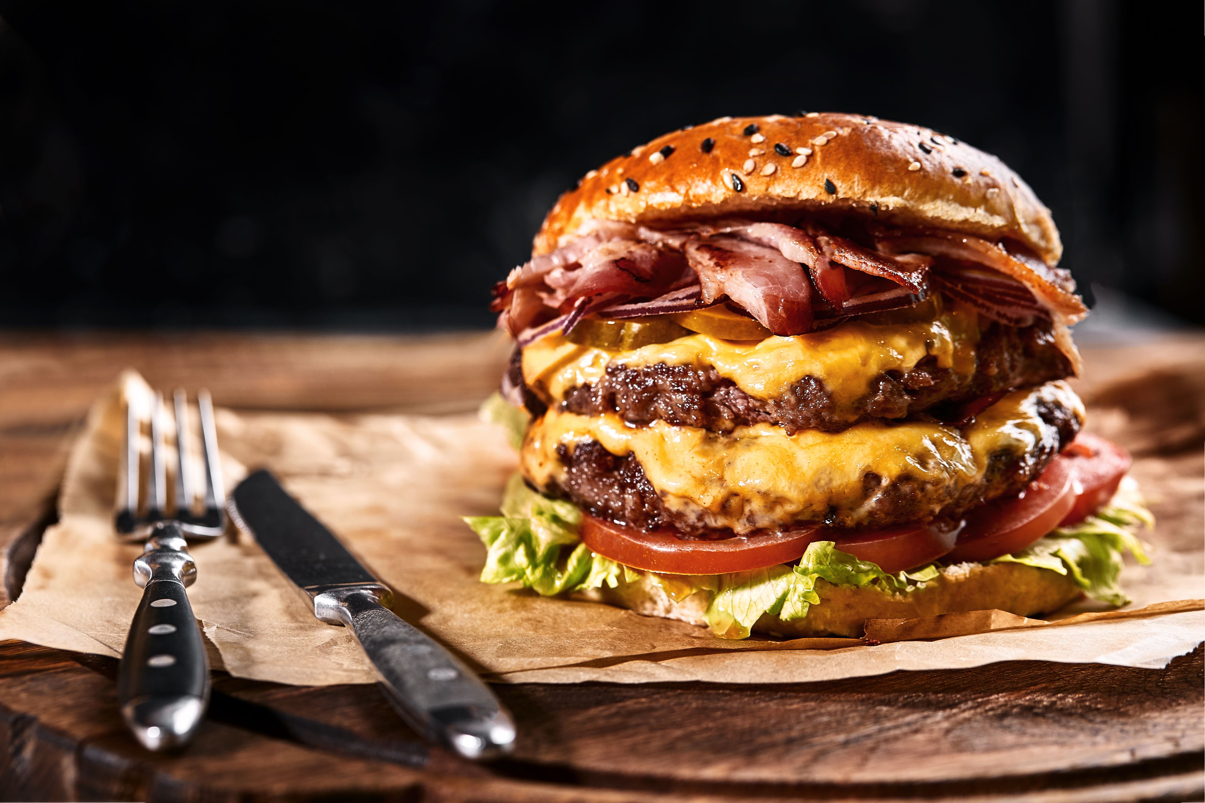 Fresh and juicy hamburger on a paper pillow with beer on a wooden table. Dark background, traditional american food. Junk food