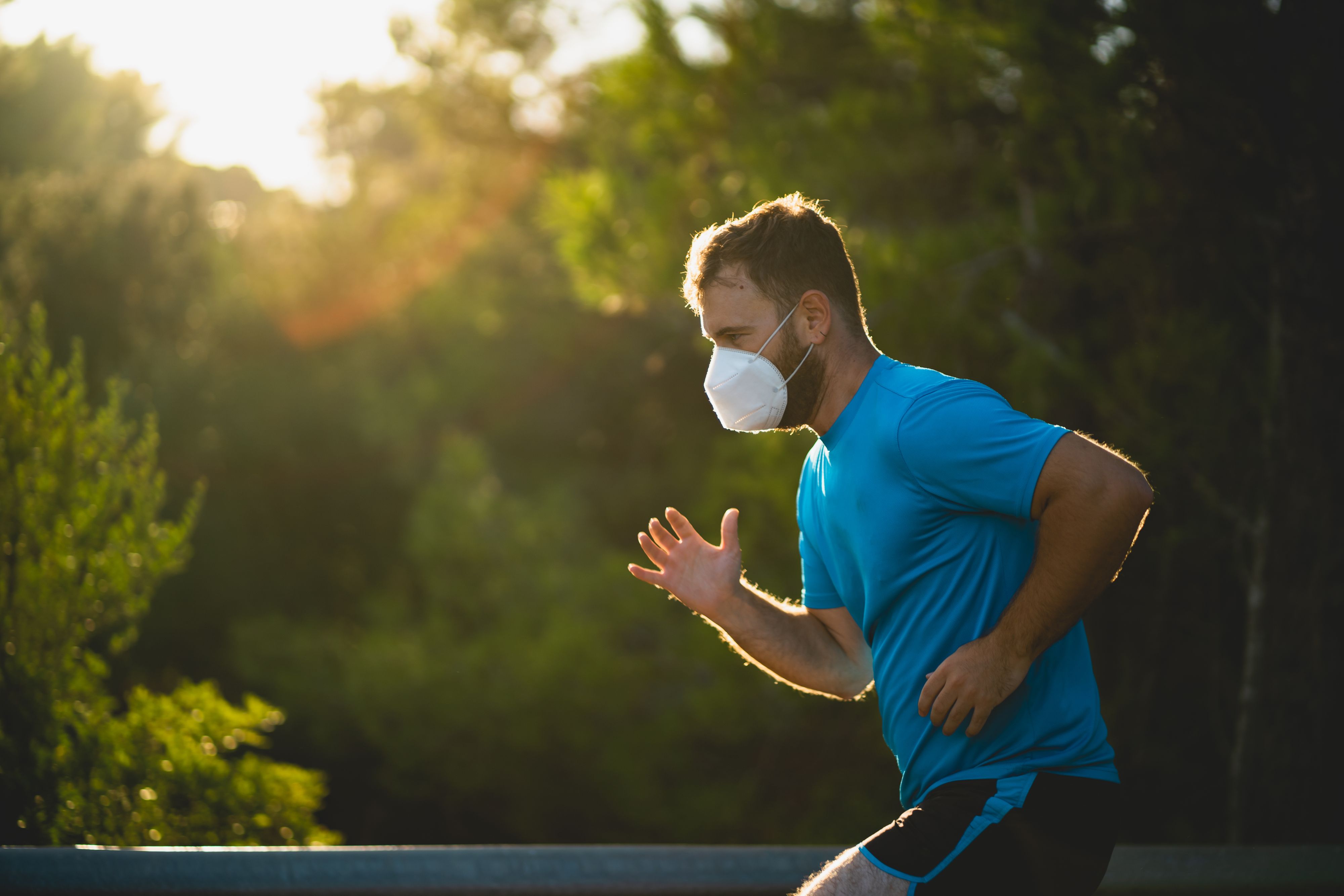Young man wearing a ffp2 surgical mask runs on a road during sunset surrounded by nature in Mallorca (Spain)